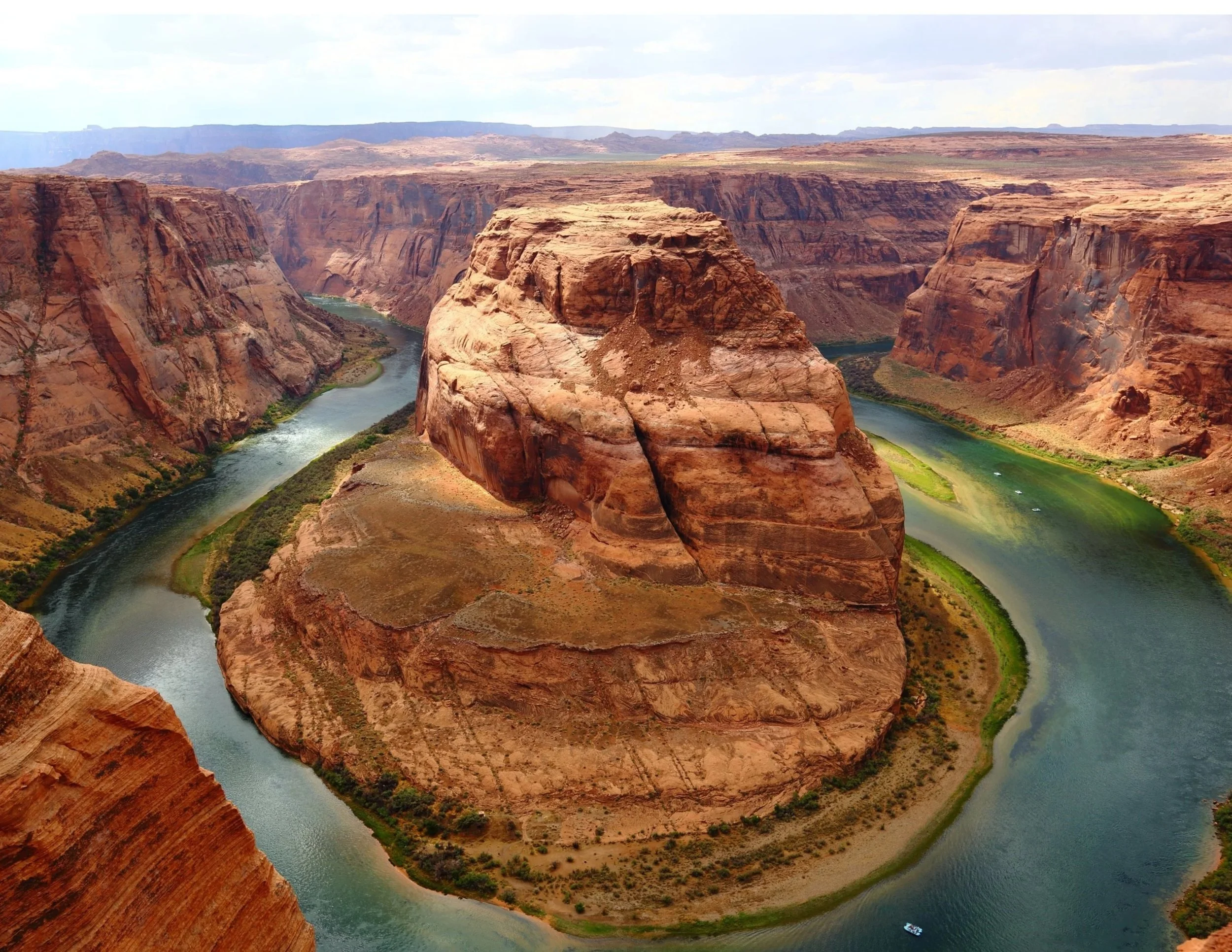 A winding river surrounds a large, flat-topped rock formation in a canyon with steep, layered cliffs.