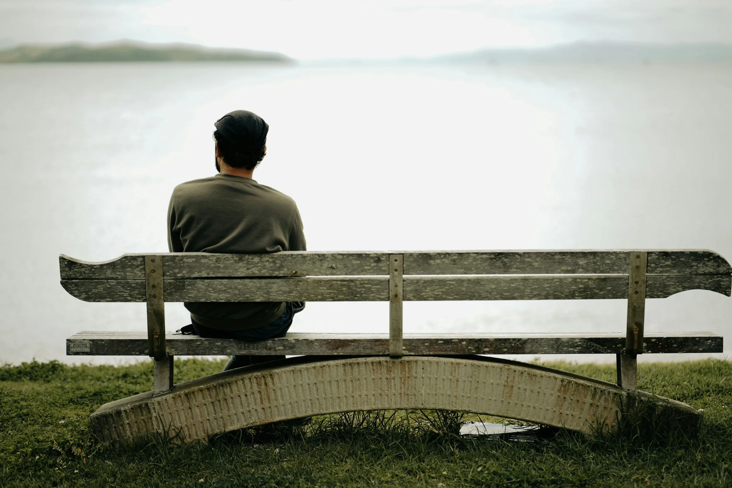 Person sitting alone on a bench looking out at the water, representing emotional exhaustion and feeling responsible for others.