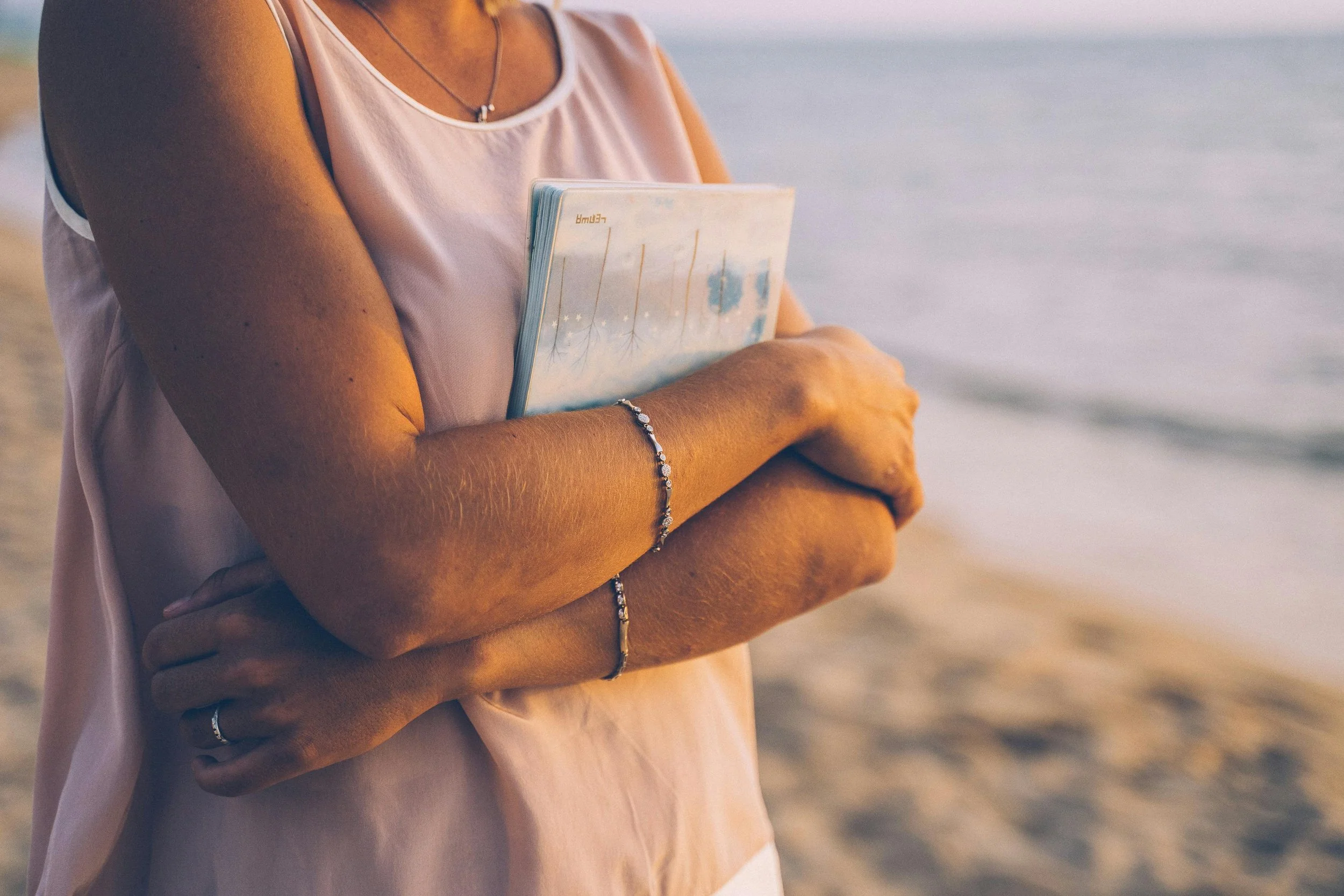 Person holding a notebook while standing near the ocean
