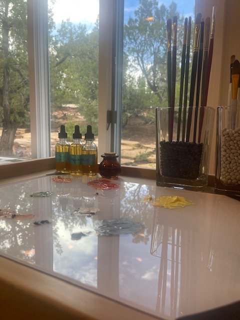 Artist's workspace with paint bottles, paintbrushes, and paint swatches by a window