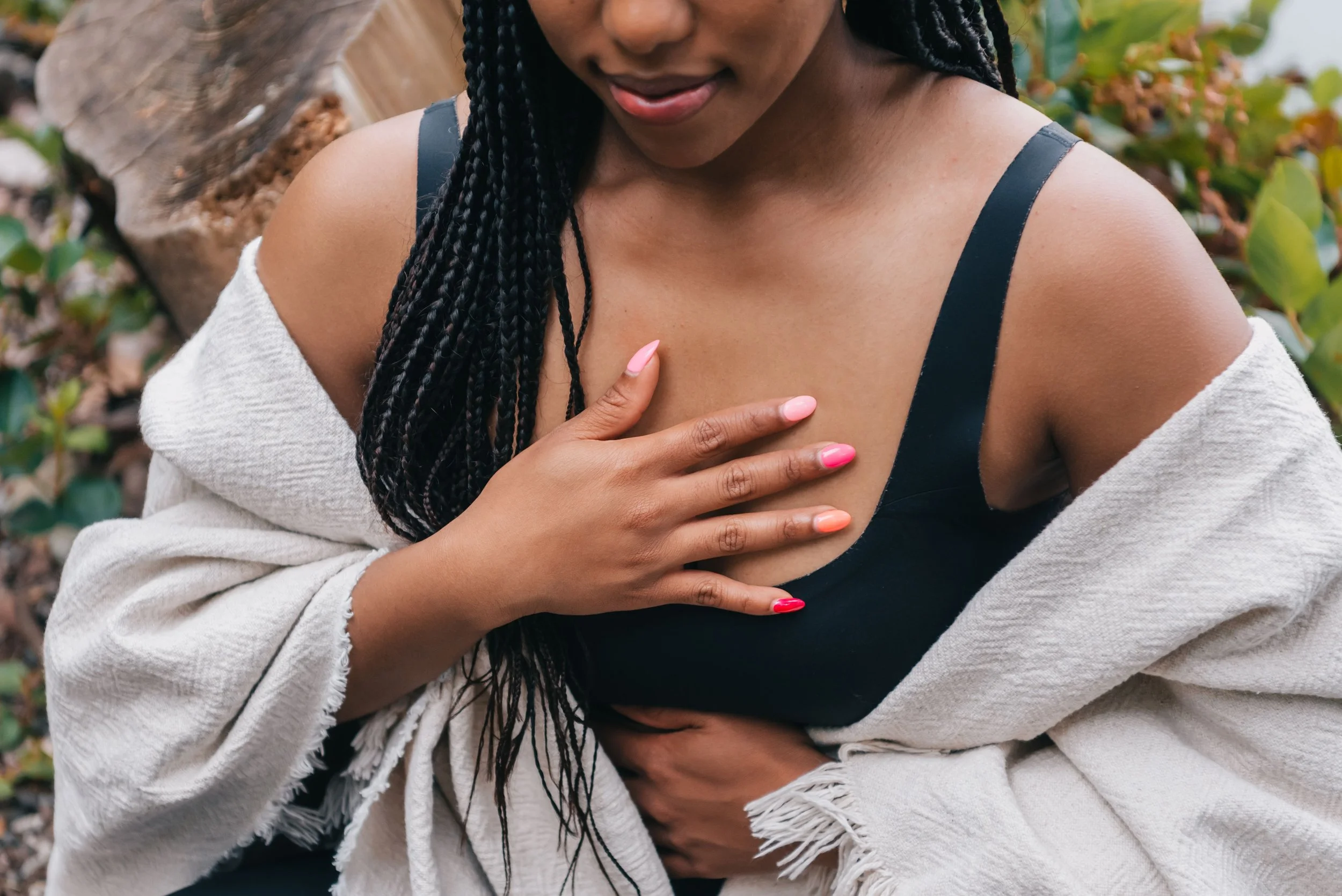 Person with long black braids standing in the forest with a hand on her chest and a hand on her upper stomach