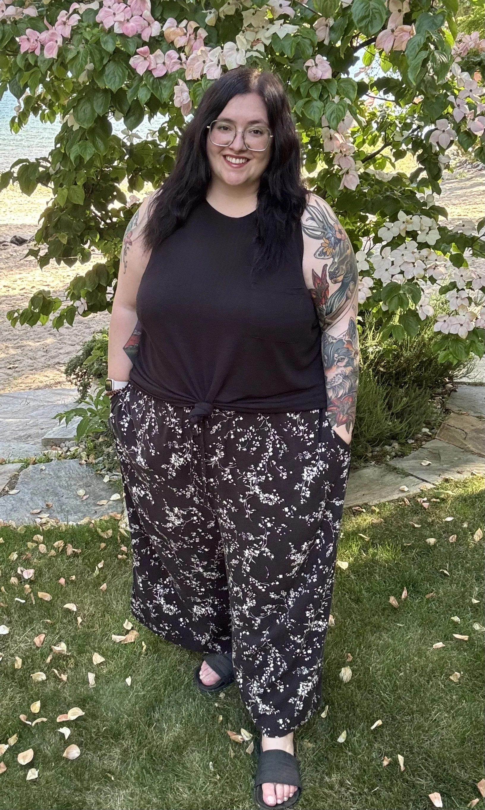 Therapist, Selena Arcovio, is standing on a grassy ledge in front of a tree with leaves on the ground