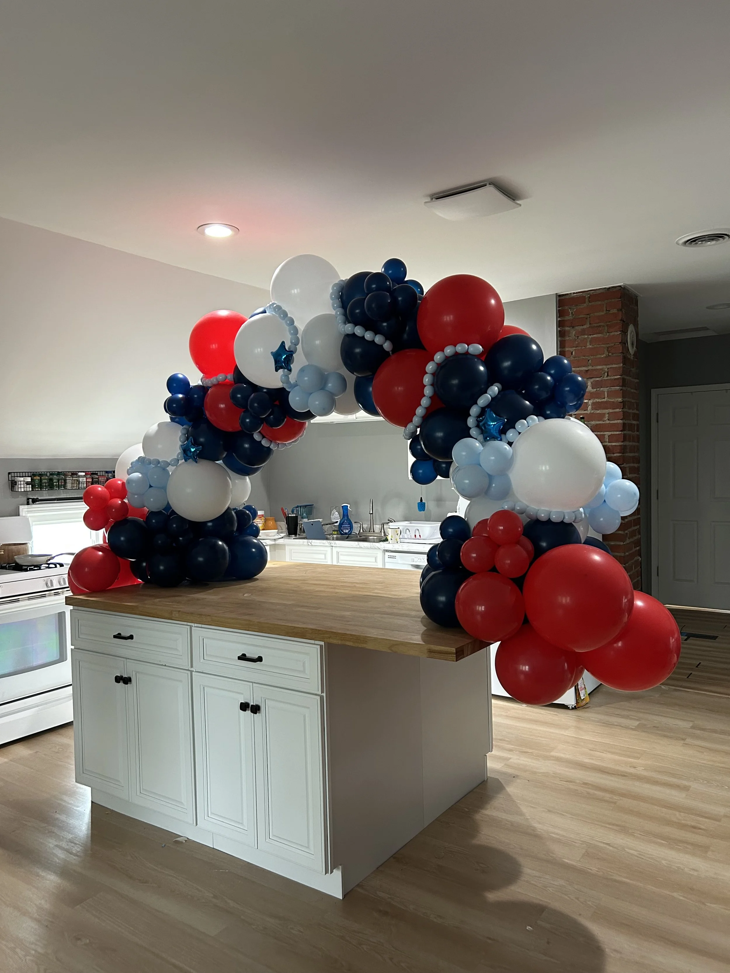 Balloon arch with red, white, and blue balloons over a kitchen island.