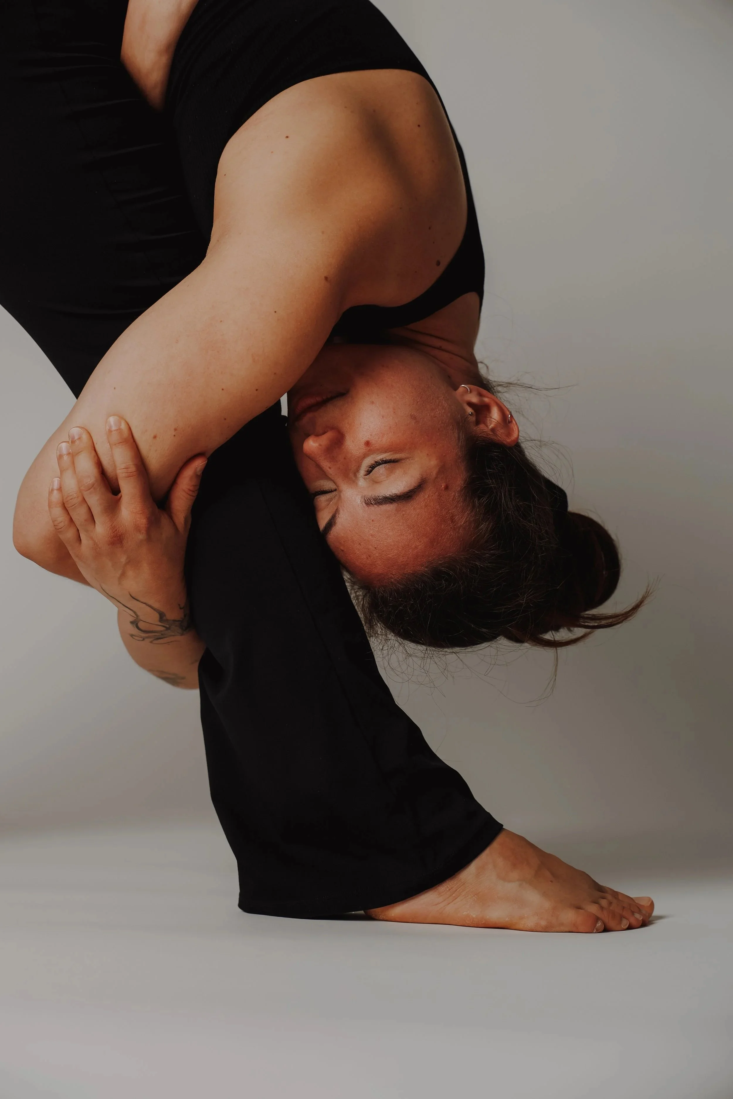 Frau in Yoga-Pose, die auf dem Boden auf Händen und Füßen steht, Kopf nach unten geneigt, Augen geschlossen, im schwarzen Outfit.