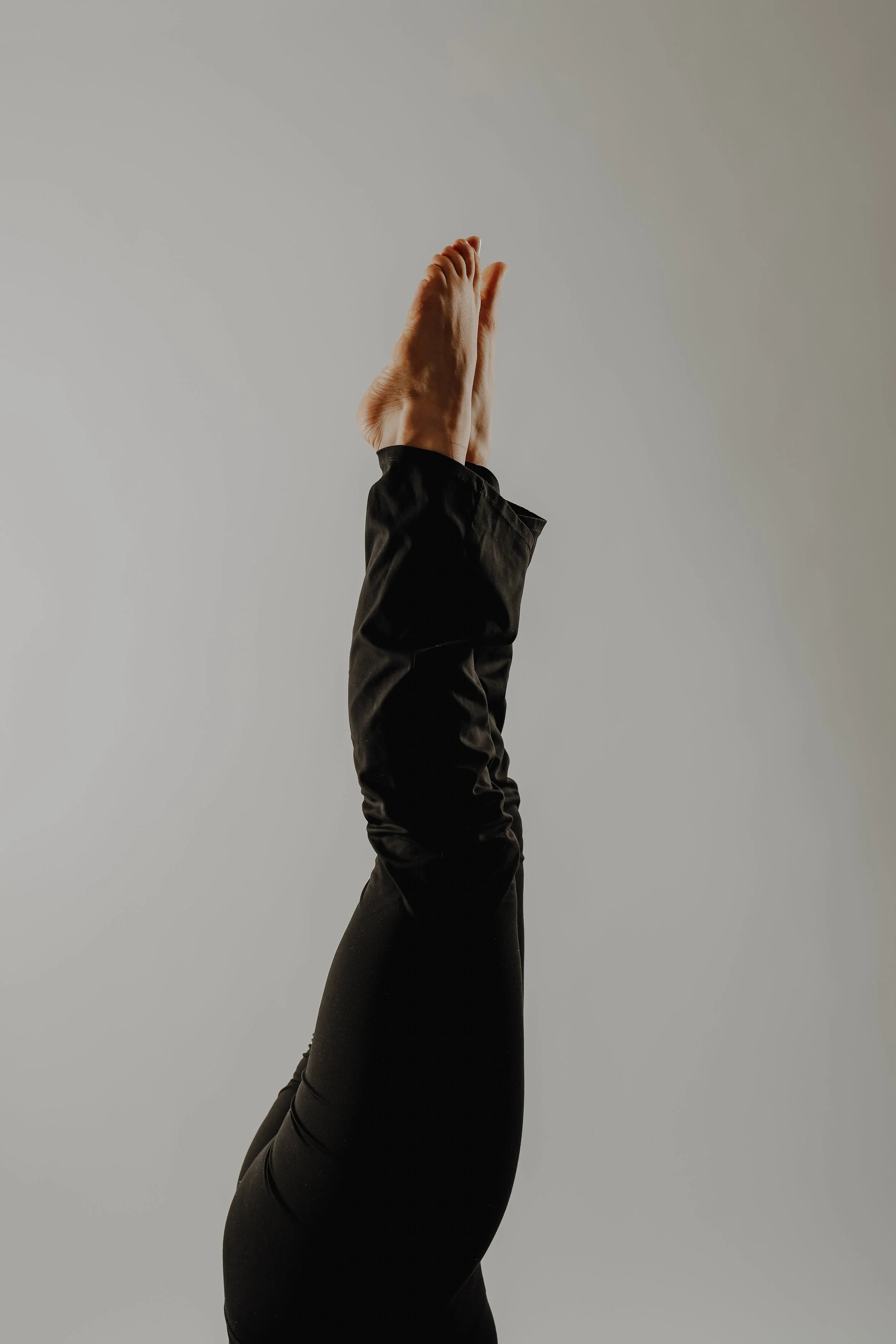 Nahaufnahme einer Person, die eine Hand im Yoga- oder Meditationsstil in Richtung Himmel hebt, Gesicht nicht sichtbar, grauer Hintergrund.