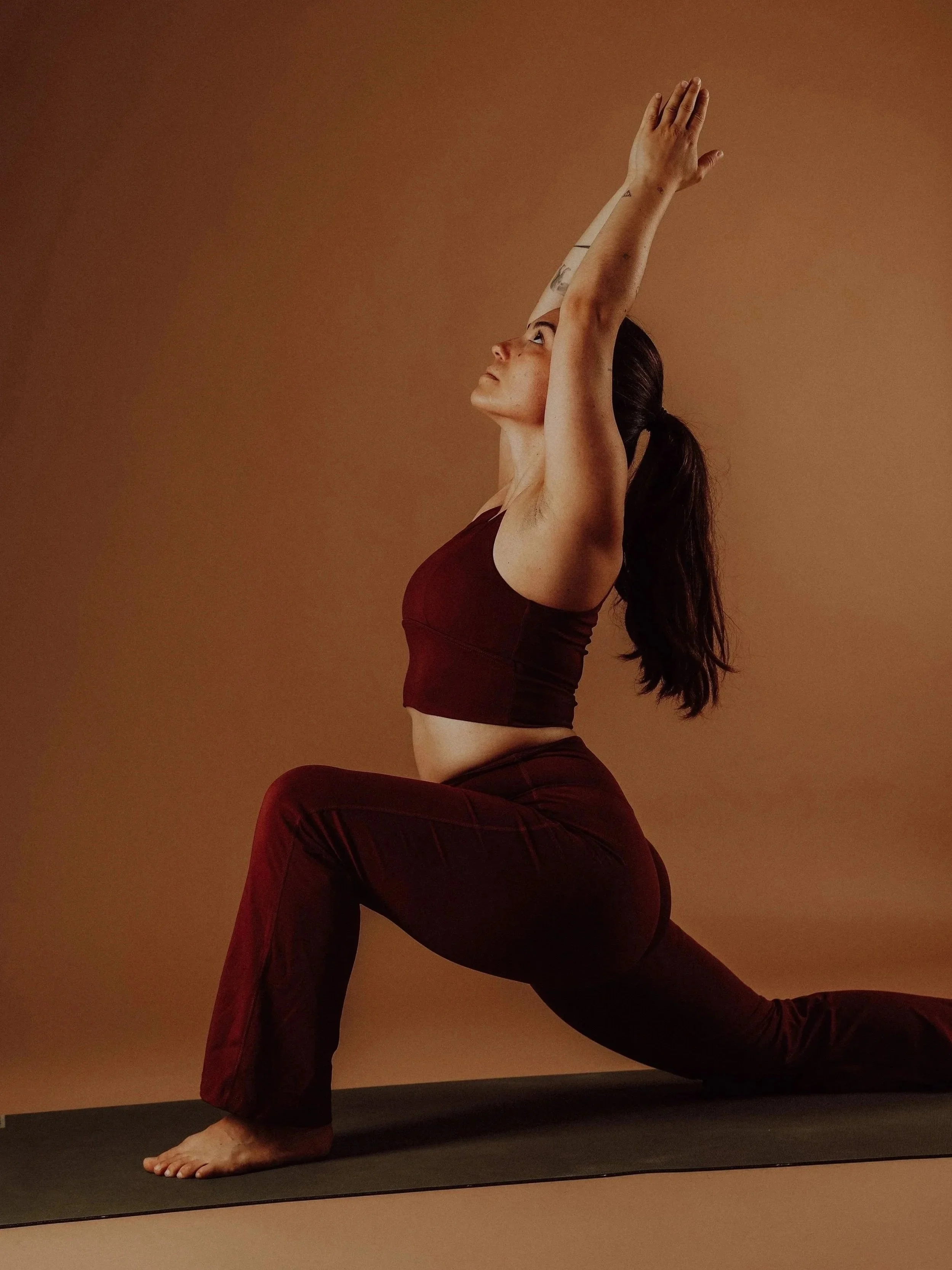 Frau in Yoga-Pose auf schwarzer Matte vor braunem Hintergrund, Hochformat