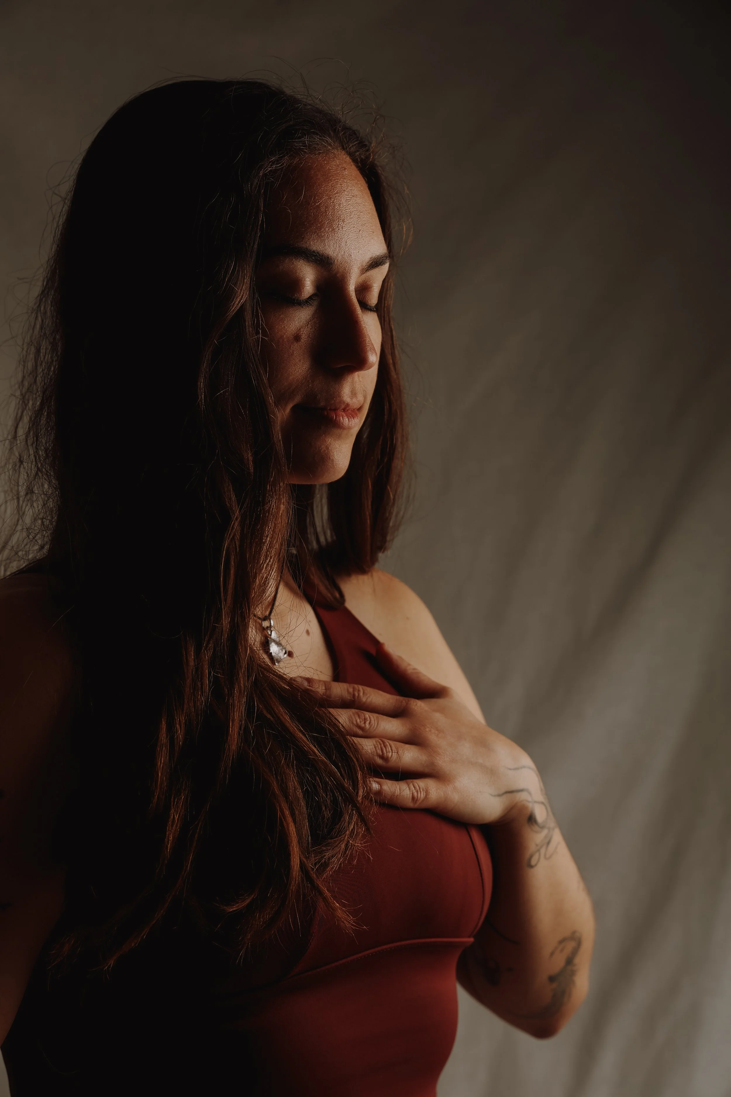 Eine Frau mit langen braunen Haaren, die die Augen geschlossen hat, die Hand auf die Brust gelegt und entspannt wirkt.