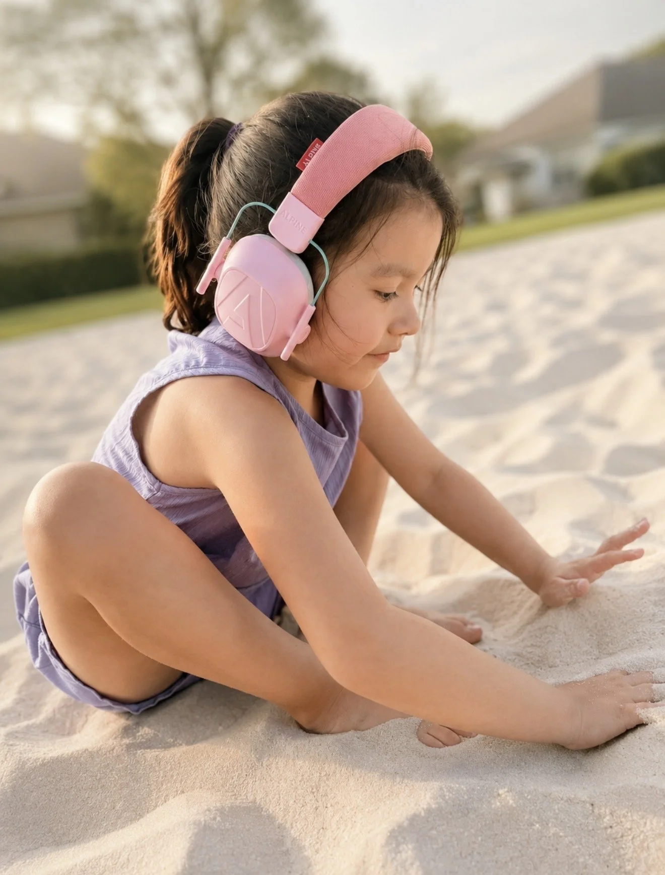 Child wearing pink sensory headphones while playing in sand