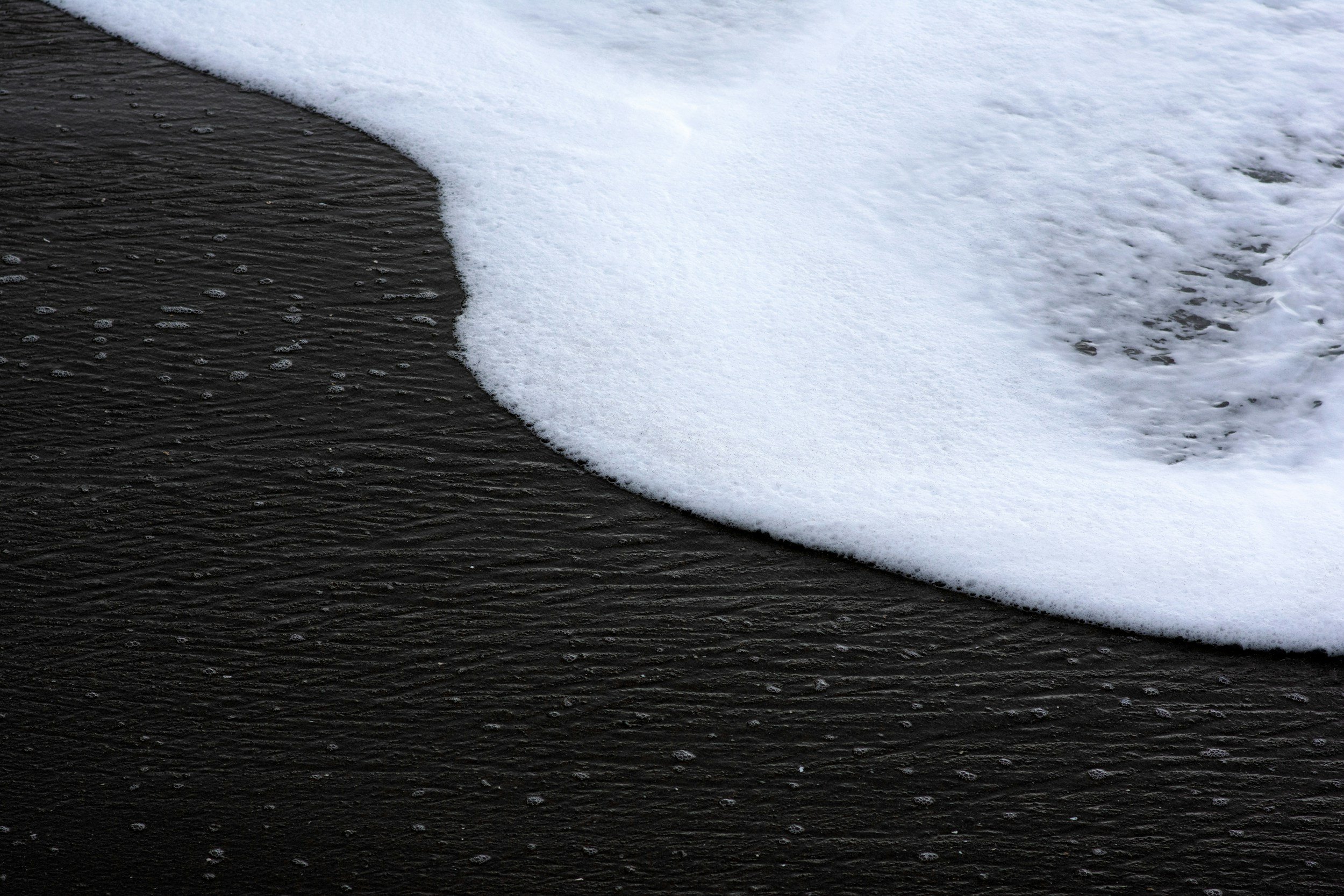 sea foam washing up on black sand creating a yin yang silhouette