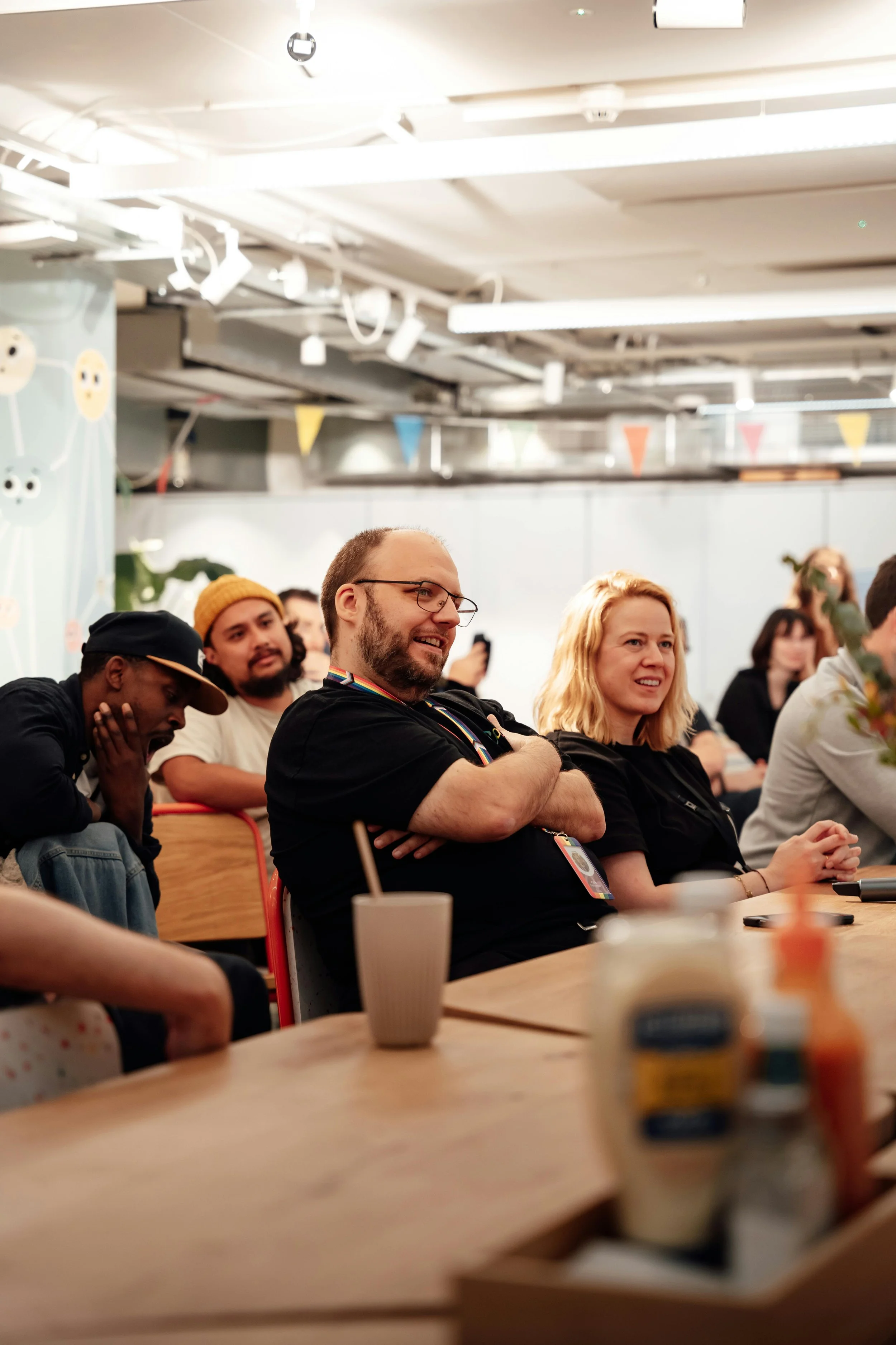 People attending a gathering or event, sitting at a table with condiments, smiling and listening attentively.