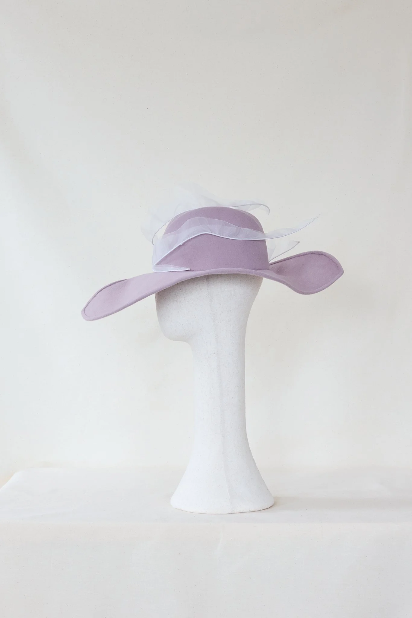 A white mannequin head wearing a light purple wide-brimmed hat with transparent ribbon details, set against a plain white background.