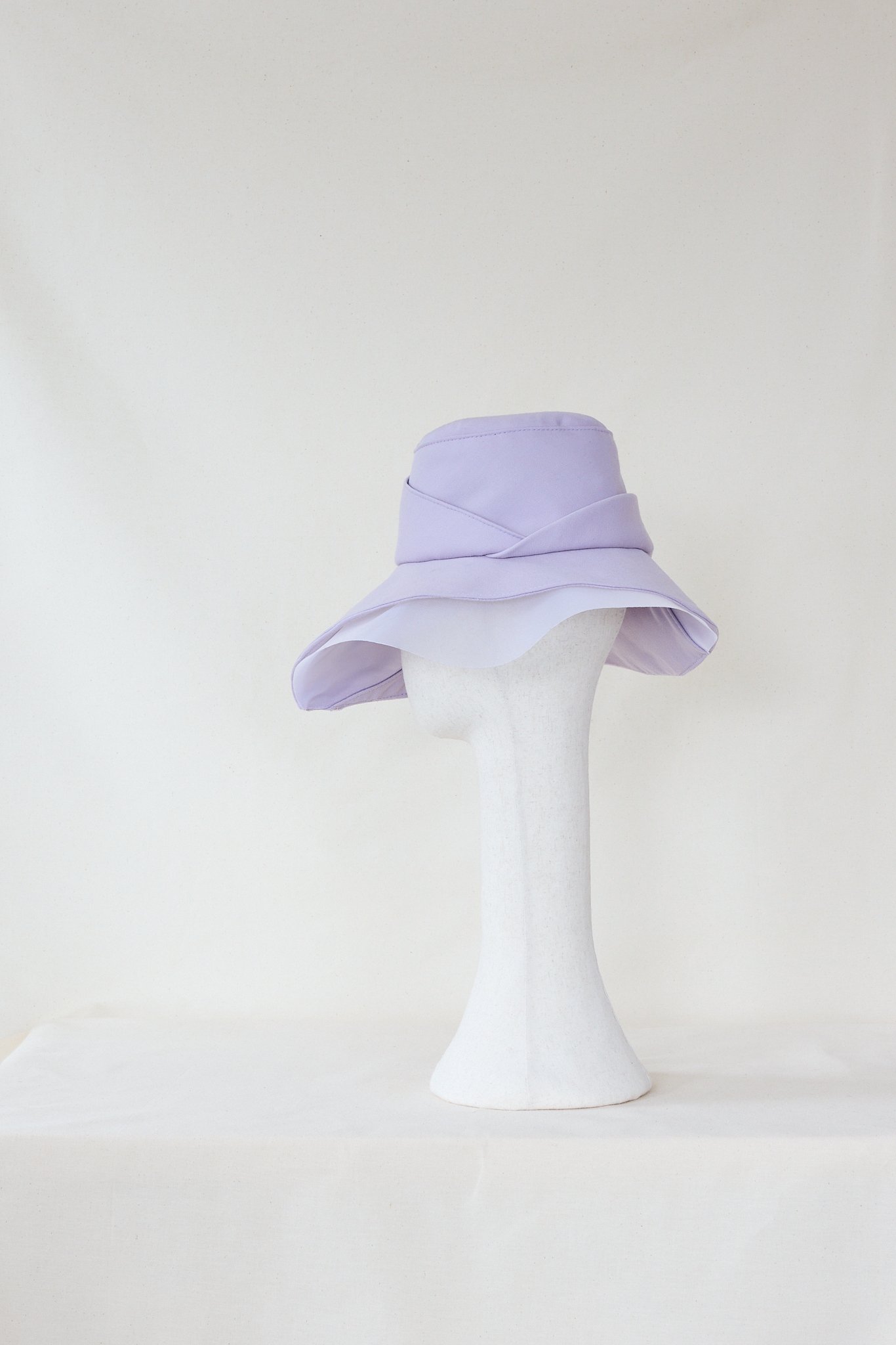 A white mannequin head without facial features wearing a light purple wide-brimmed hat.