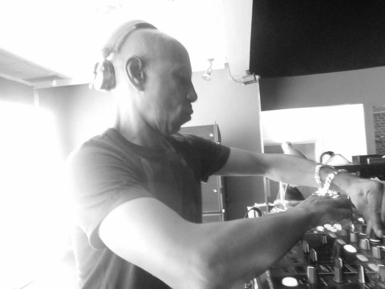 A male DJ wearing headphones, operating DJ equipment in a dimly lit room.