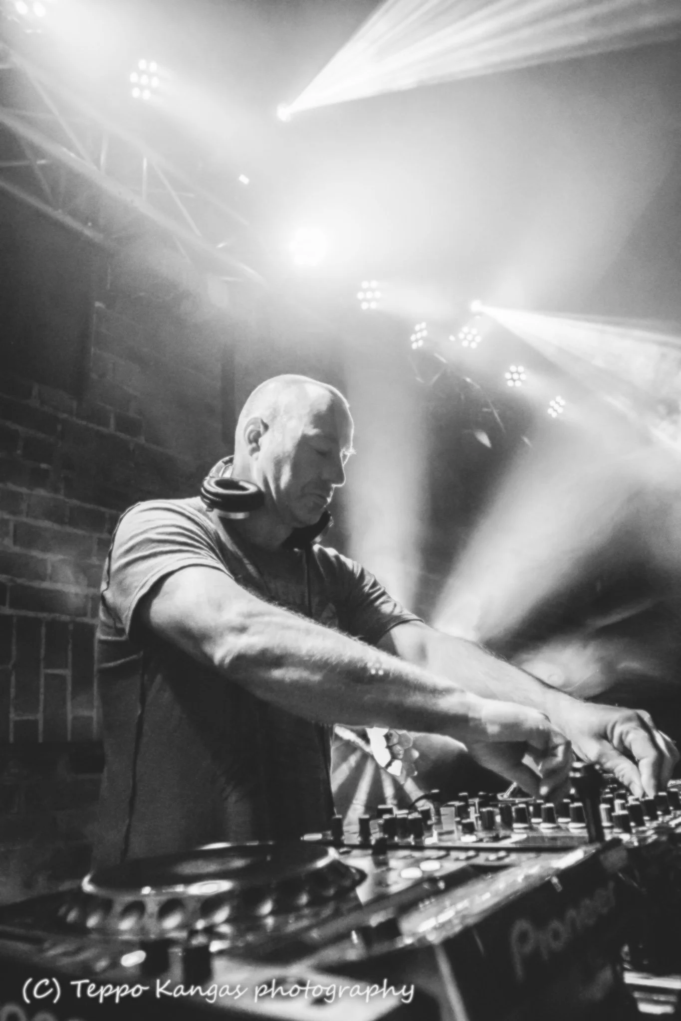 A DJ wearing headphones is playing music on a DJ mixer in a nightclub, illuminated by stage lights.