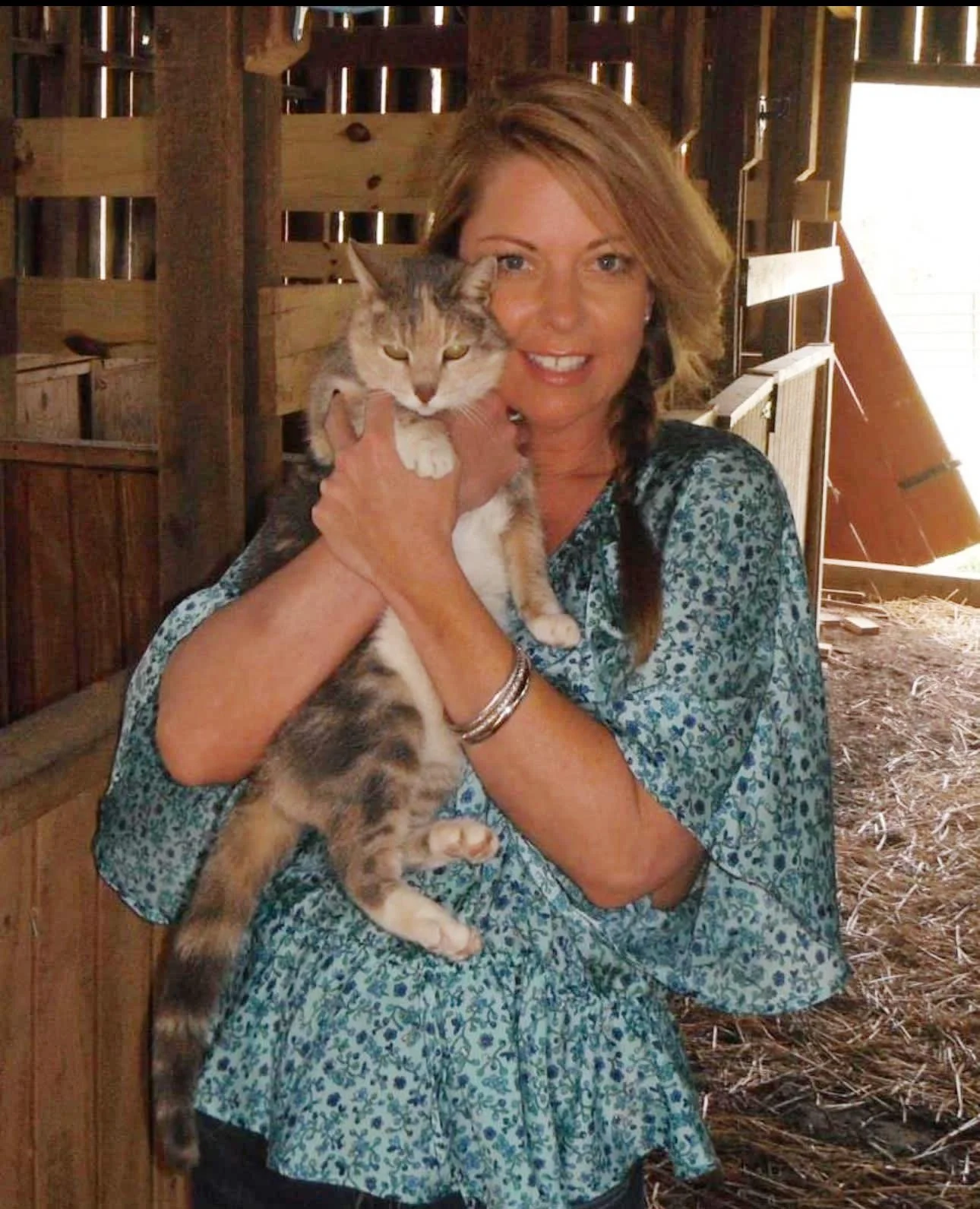 Christy, your Pet Nanny, with light brown hair holding a tabby cat inside a barn with wooden walls.