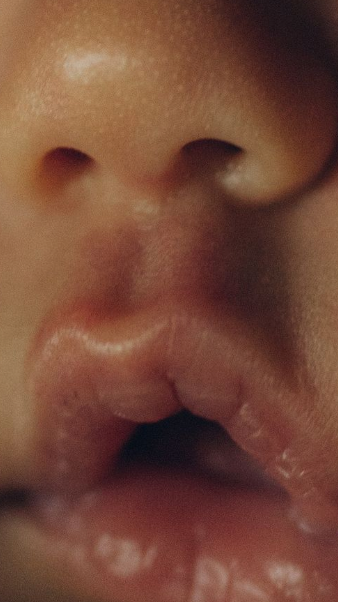 Close-up of a baby's face with a focus on the nose, lips, and tongue sticking out.