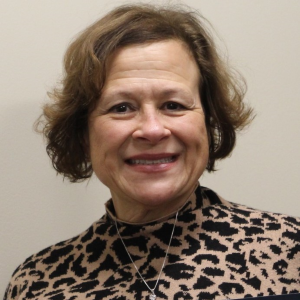 A woman smiling, wearing a leopard print top, with curly hair and earrings.