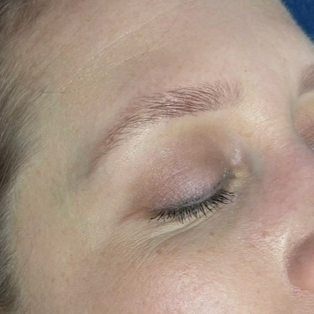 Close-up of a person's closed eye, showing light makeup and well-groomed eyebrow.