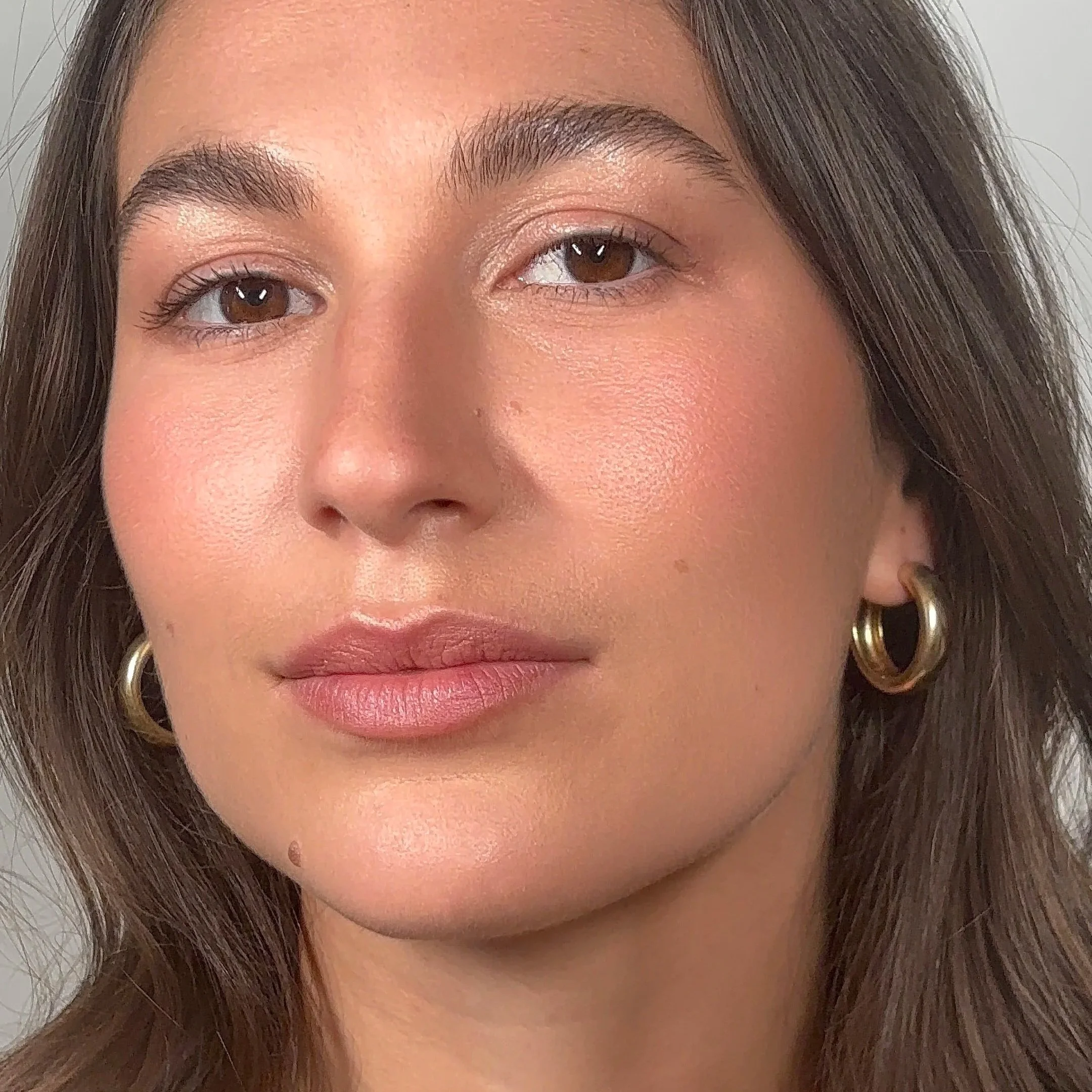 Close-up of a woman's face showing her brown eyes, eyebrows, nose, and lips, with brown hair and hoop earrings.