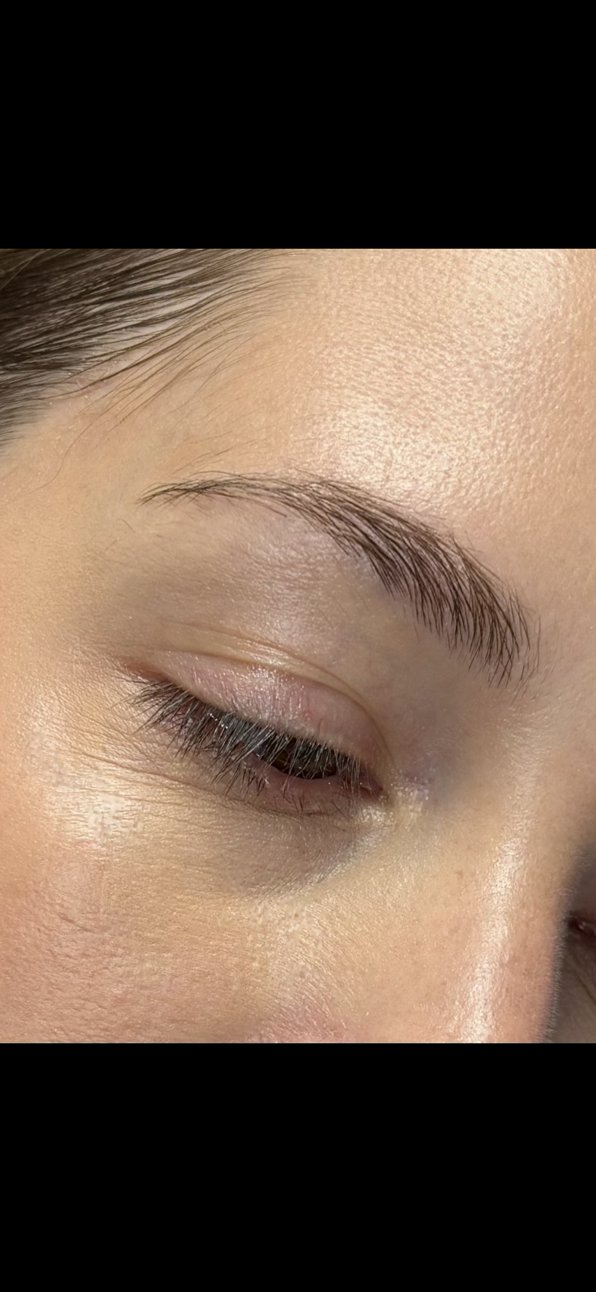 Close-up of a person's eye with groomed eyebrow, long eyelashes, and smooth skin, with the eye closed.