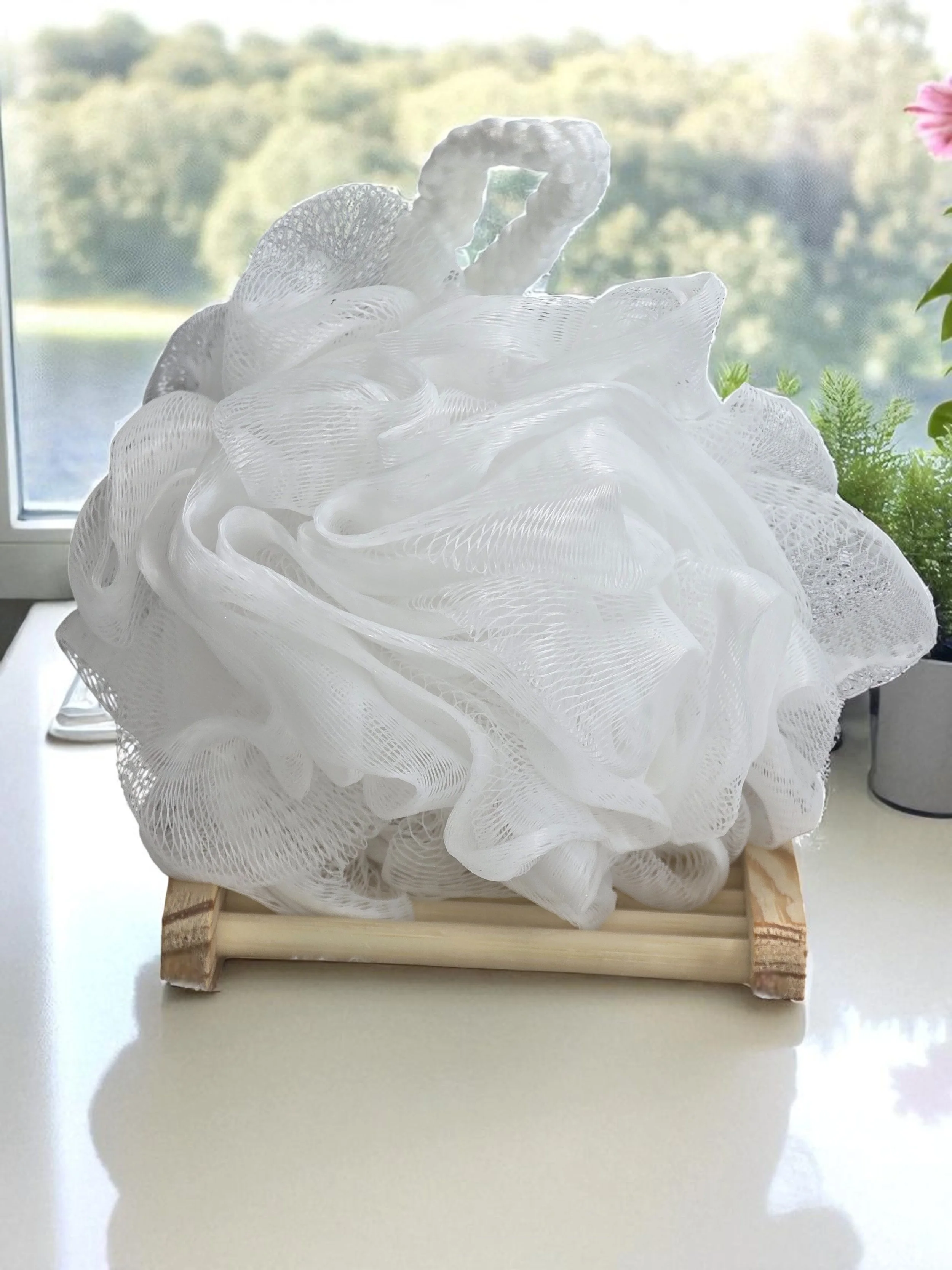 White decorative soap foam arranged on a wooden tray near a window with a scenic view of trees and water outside.
