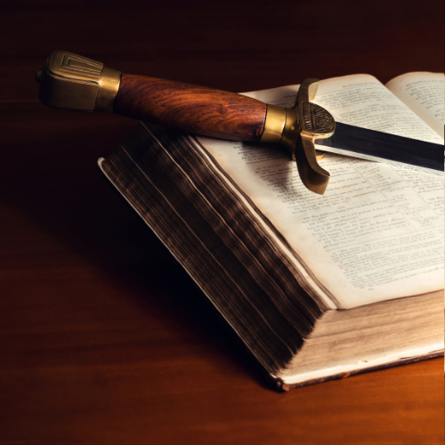 A sword resting on an open book on a wooden surface.