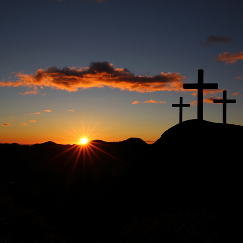 Sunset over hills with three crosses on a hill in silhouette.