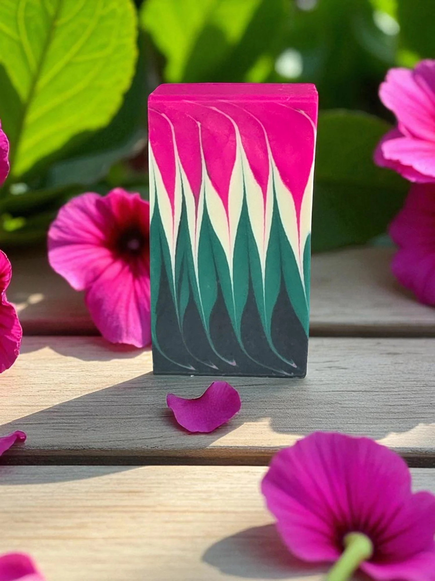 Colorful rectangular box with a pink, white, and teal abstract pattern, placed on a wooden surface surrounded by pink petal flowers and green leaves.