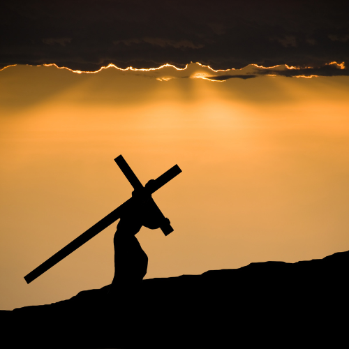 Silhouette of a person carrying a cross on a hill at sunset with a cloudy sky.