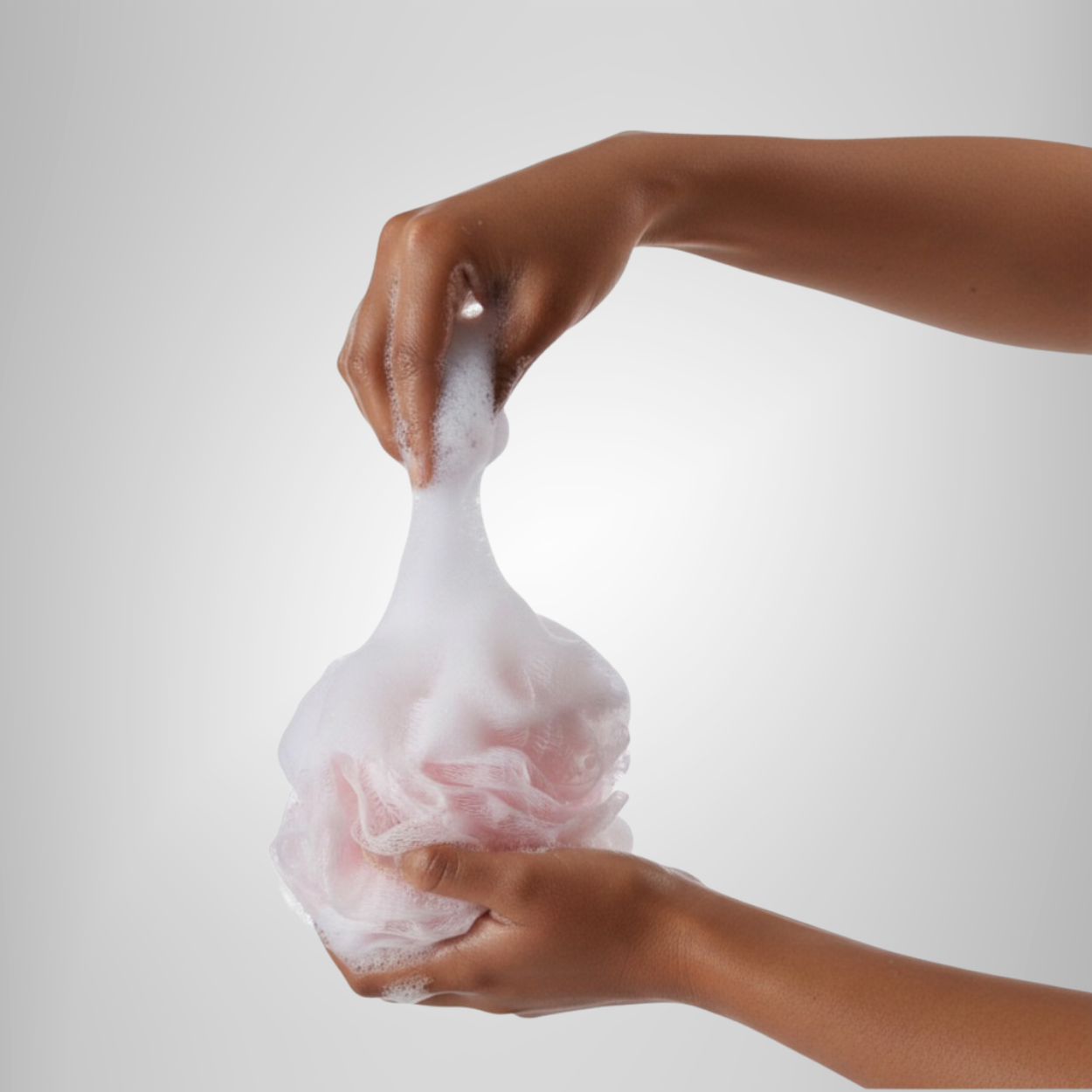 Two hands holding a pink and white bath sponge creating soap suds, hands are wet.