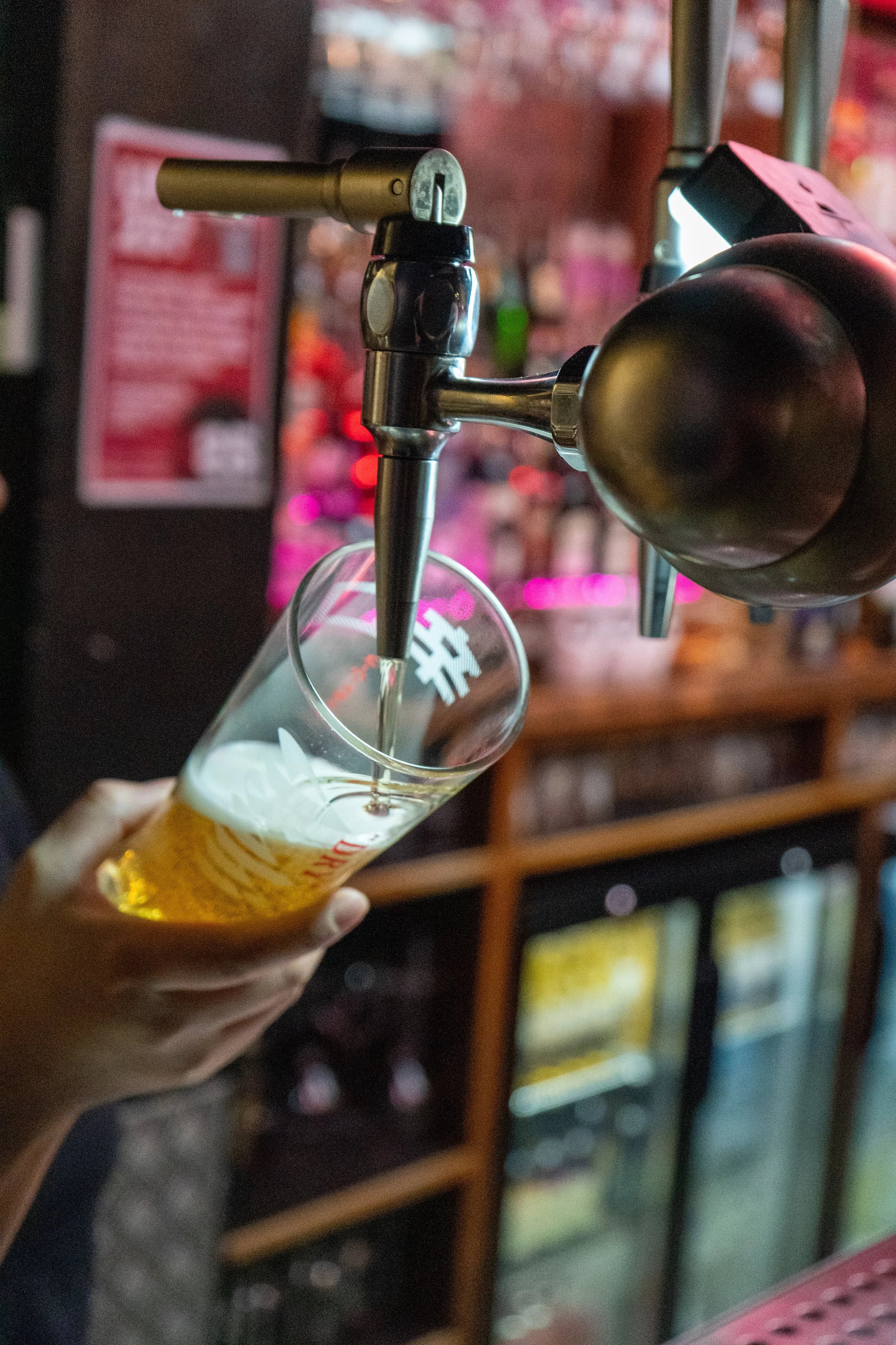 A person holding a glass of beer being poured from a tap at a bar.