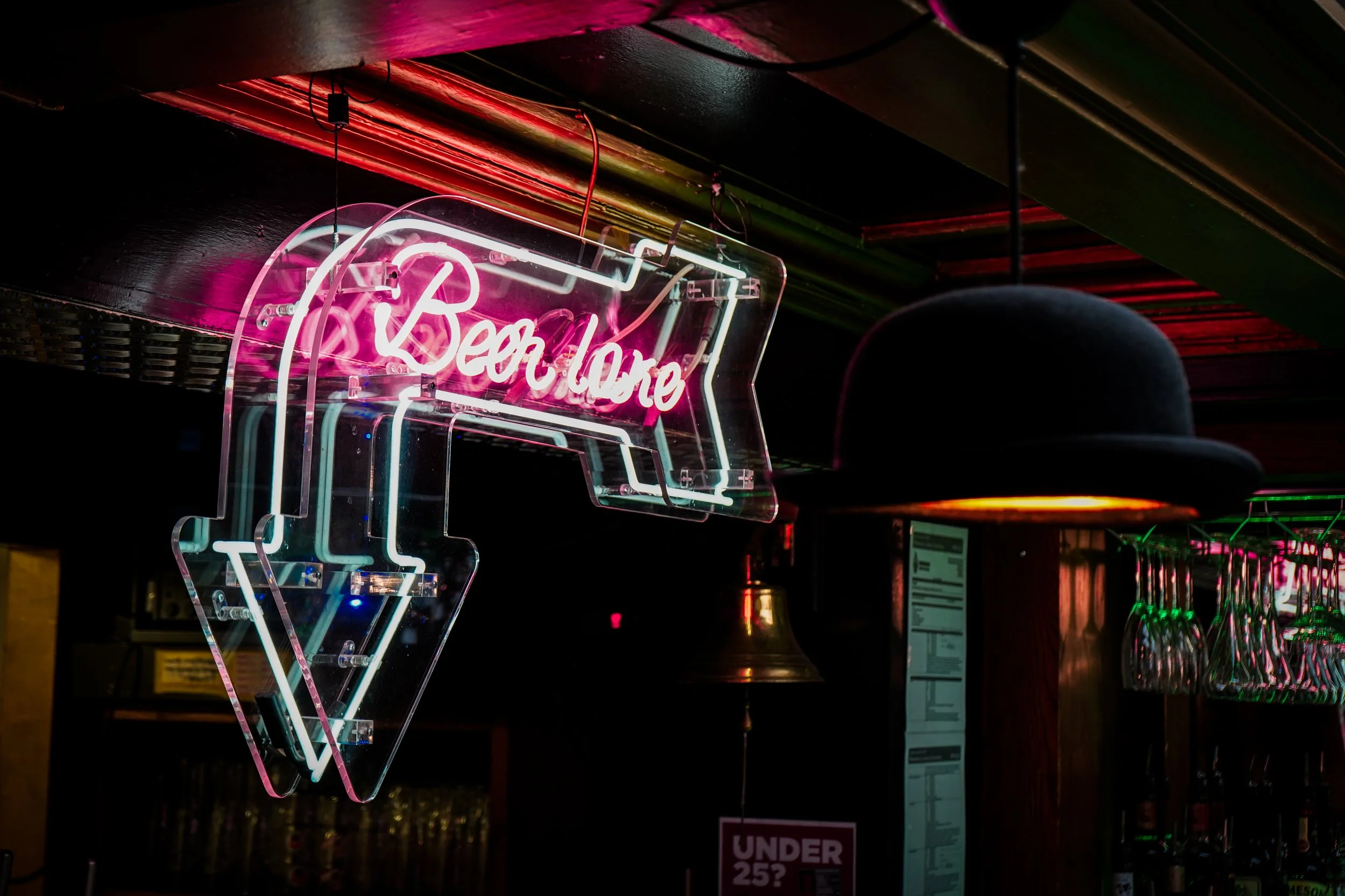 Neon sign shaped like an ice cream cone with the words 'Beer. more' in pink and white lights, hanging above a bar area.