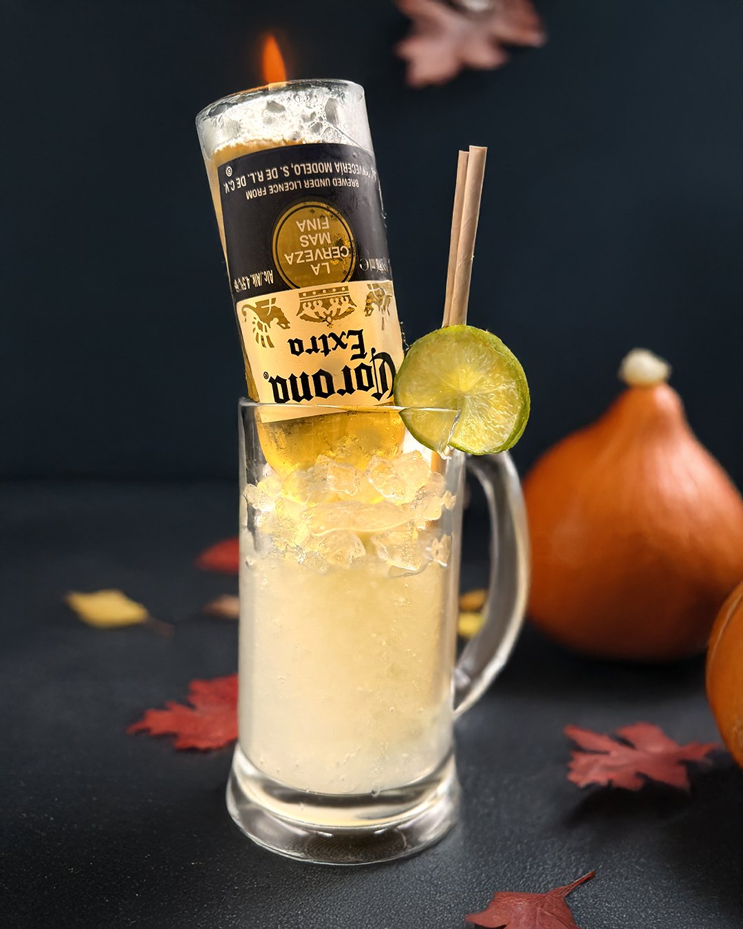 A Mojito with a Corona beer in the bottle up ended. A glass Tankard with handle filled with crushed ice and a lime wheel on the rim. There is a straw in the drink, and the background features a halloween theme with autumn leaves.