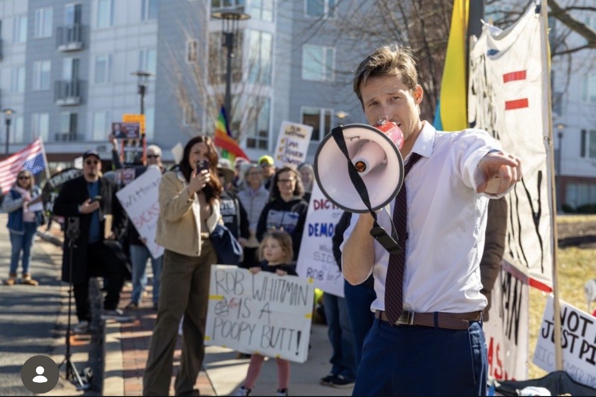 Tim Cywinski holding a bullhorn speaking at a rally protesting Rob Wittman.