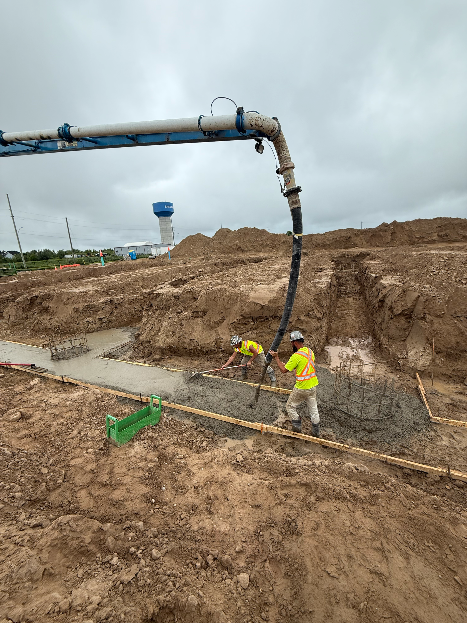 Construction workers pouring concrete foundation with a large overhead boom. 