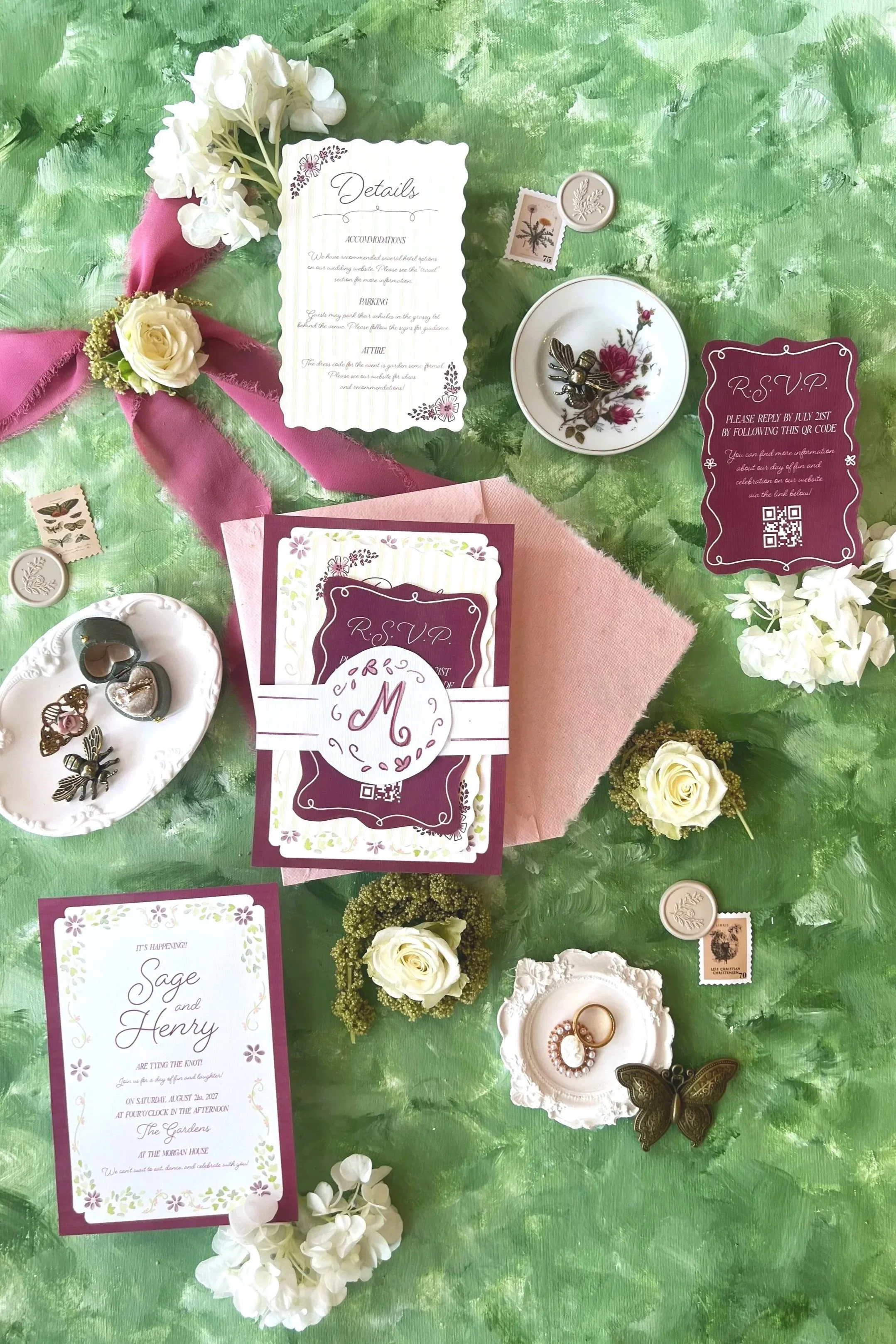 Wedding invitation suite with RSVP cards, floral decorations, jewelry, and decorative items arranged on a green textured background.