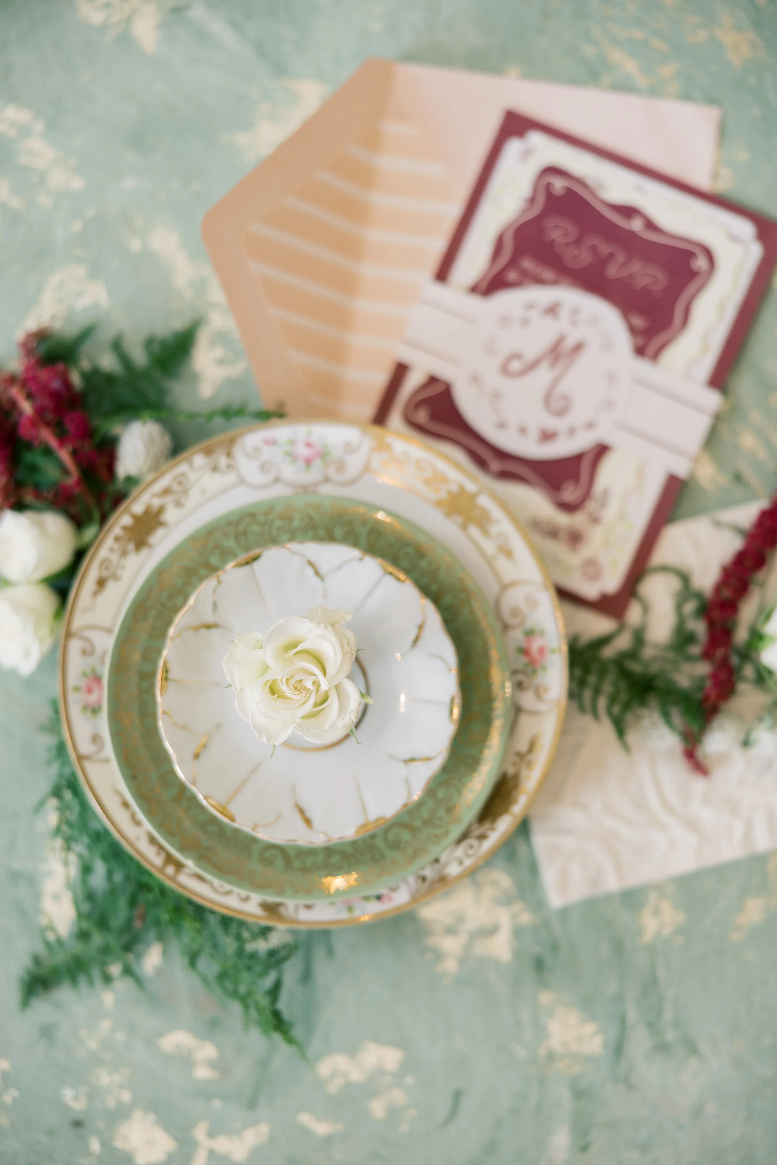 A vintage tiered cake with white icing and white roses on top, surrounded by floral arrangements, vintage cards, and envelopes on a pastel green surface.