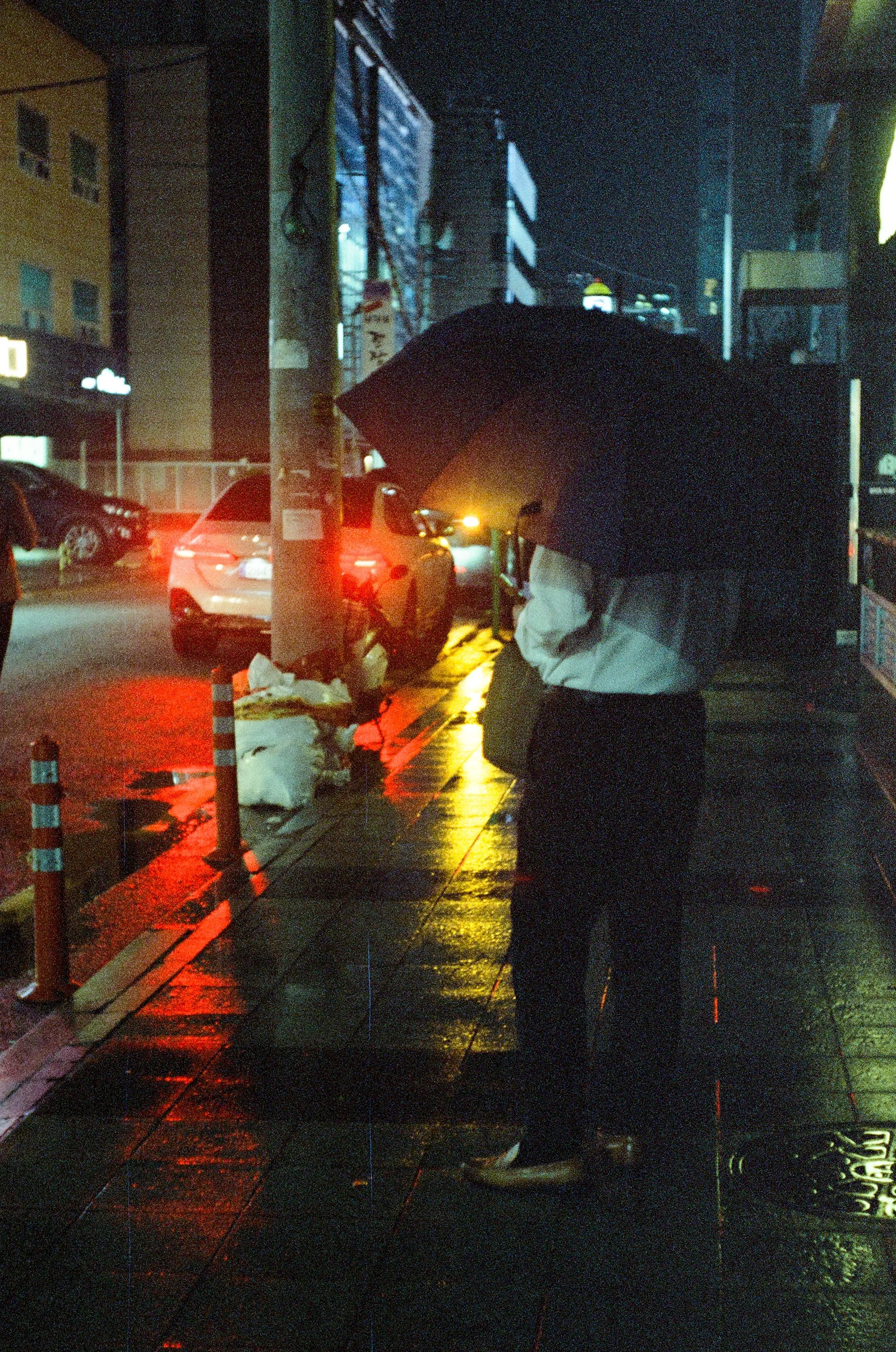 Film photo of a man in the rain at night covered by his umbrella