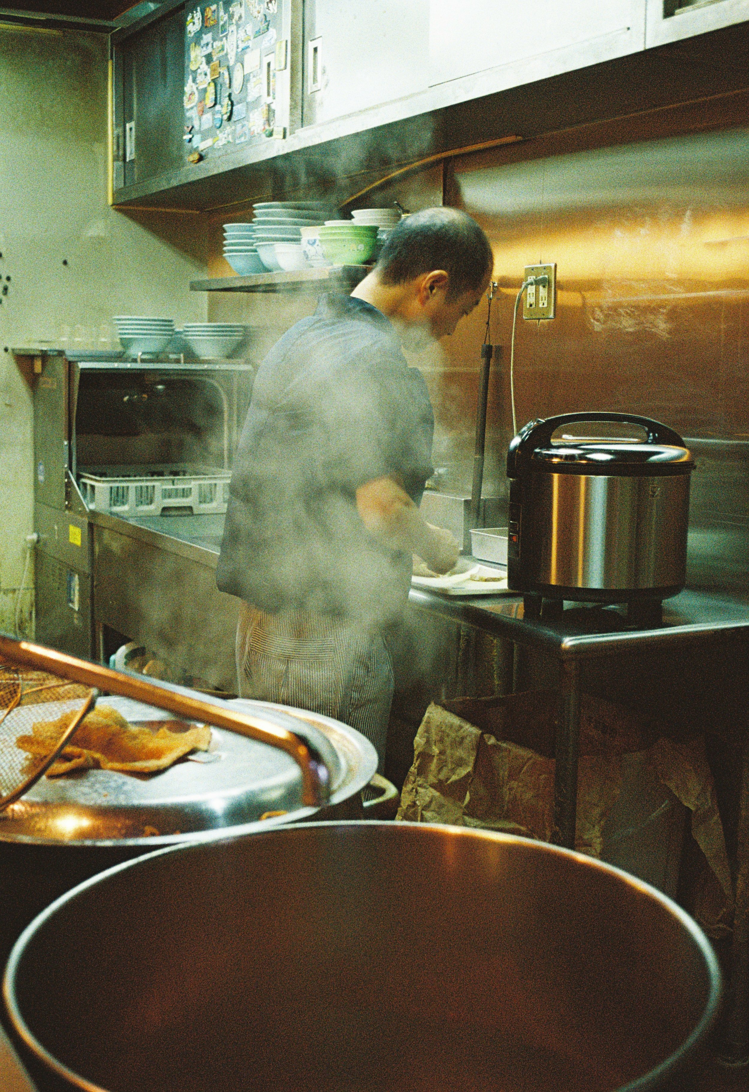 A person cooking in a kitchen with steam rising around them, surrounded by bowls and kitchen appliances.