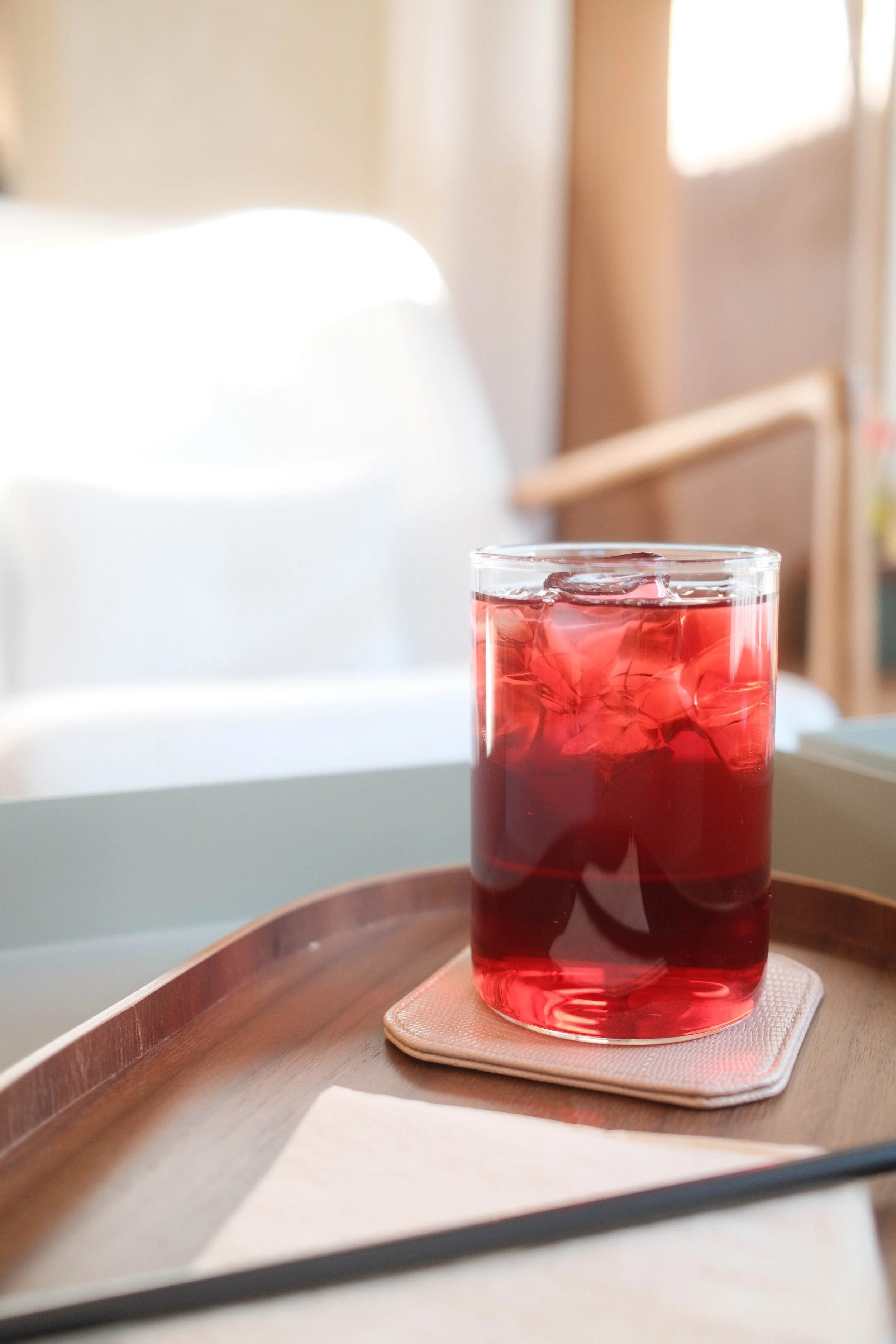 A glass of red iced beverage placed on a pink napkin on a round wooden tray.