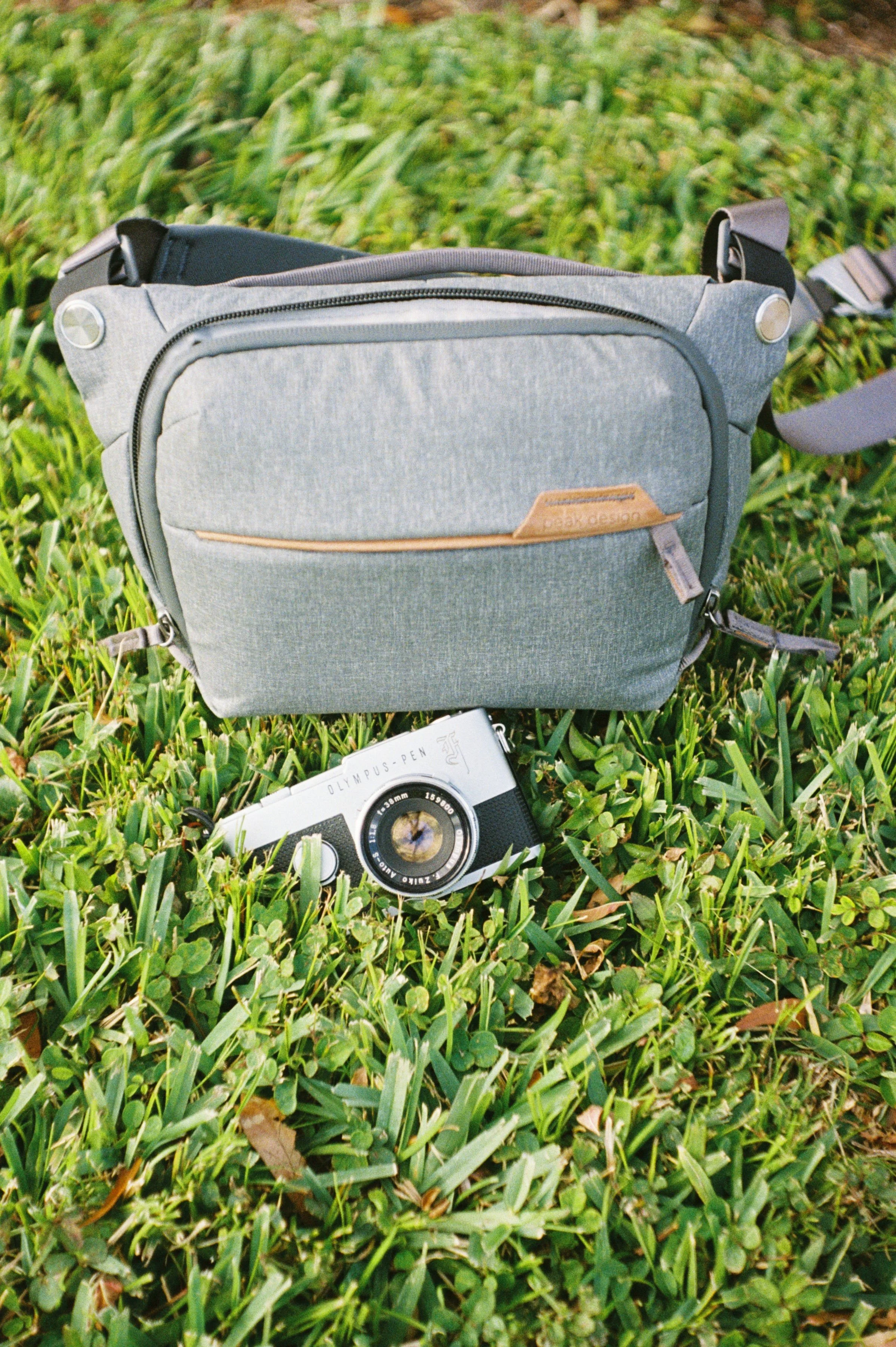 A film photo of the Olympus Pen F film camera and a camera bag on grass