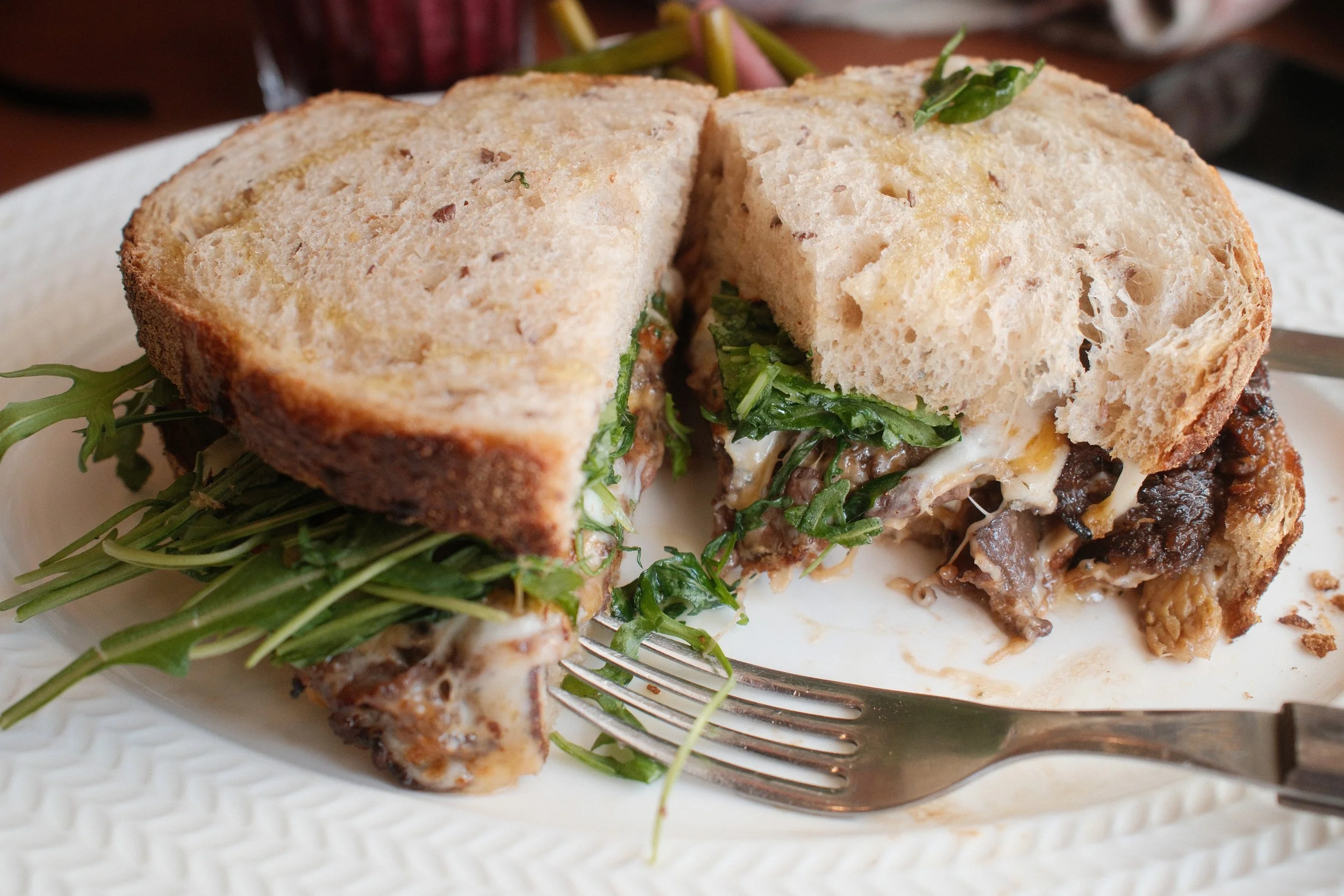 A club sandwich with toasted bread, leafy greens, cheese, and sliced meat on a white plate.