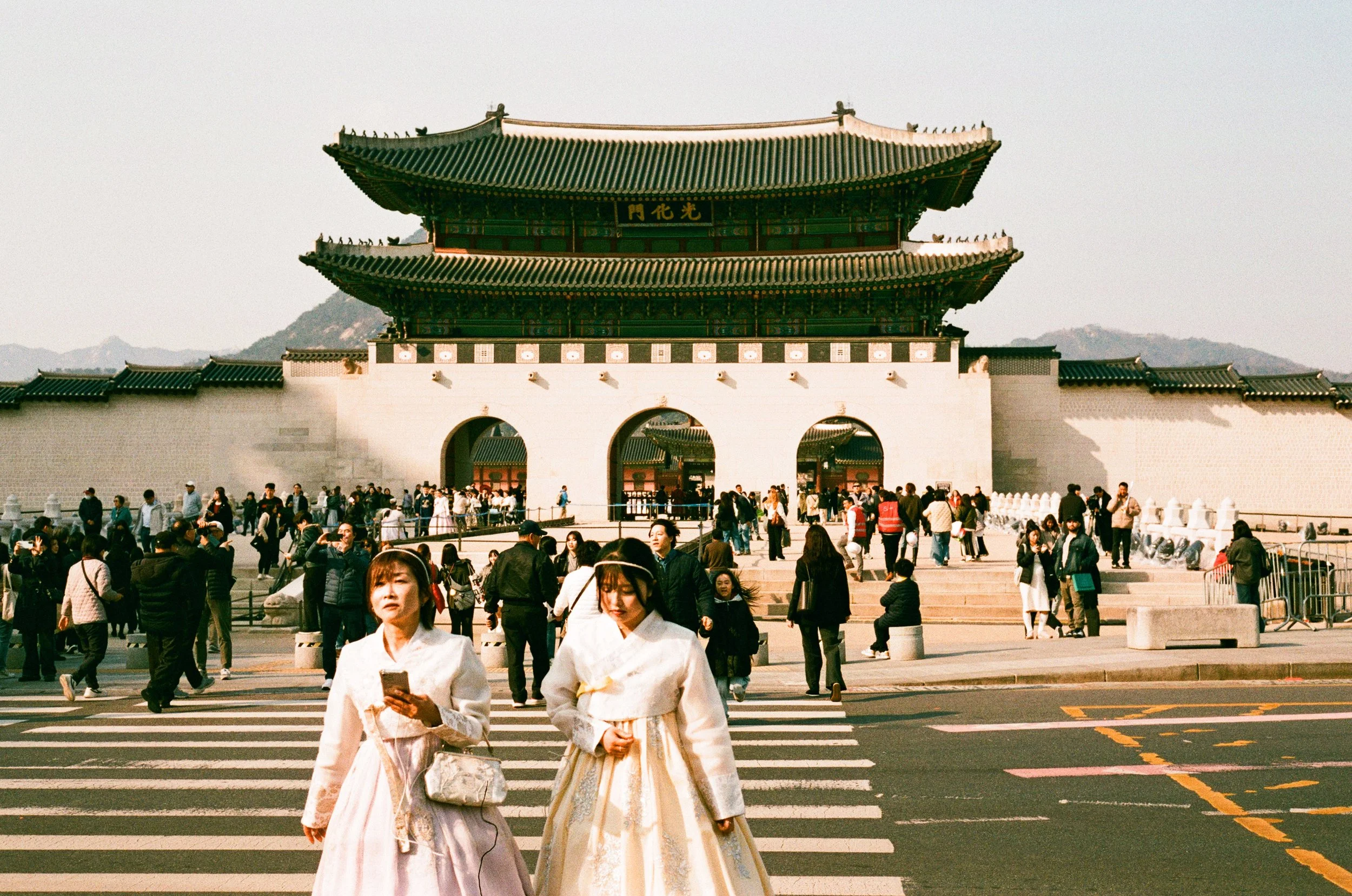 Two women walking away from the Seoul Palace while dressed in Traditional Korean Hanbok