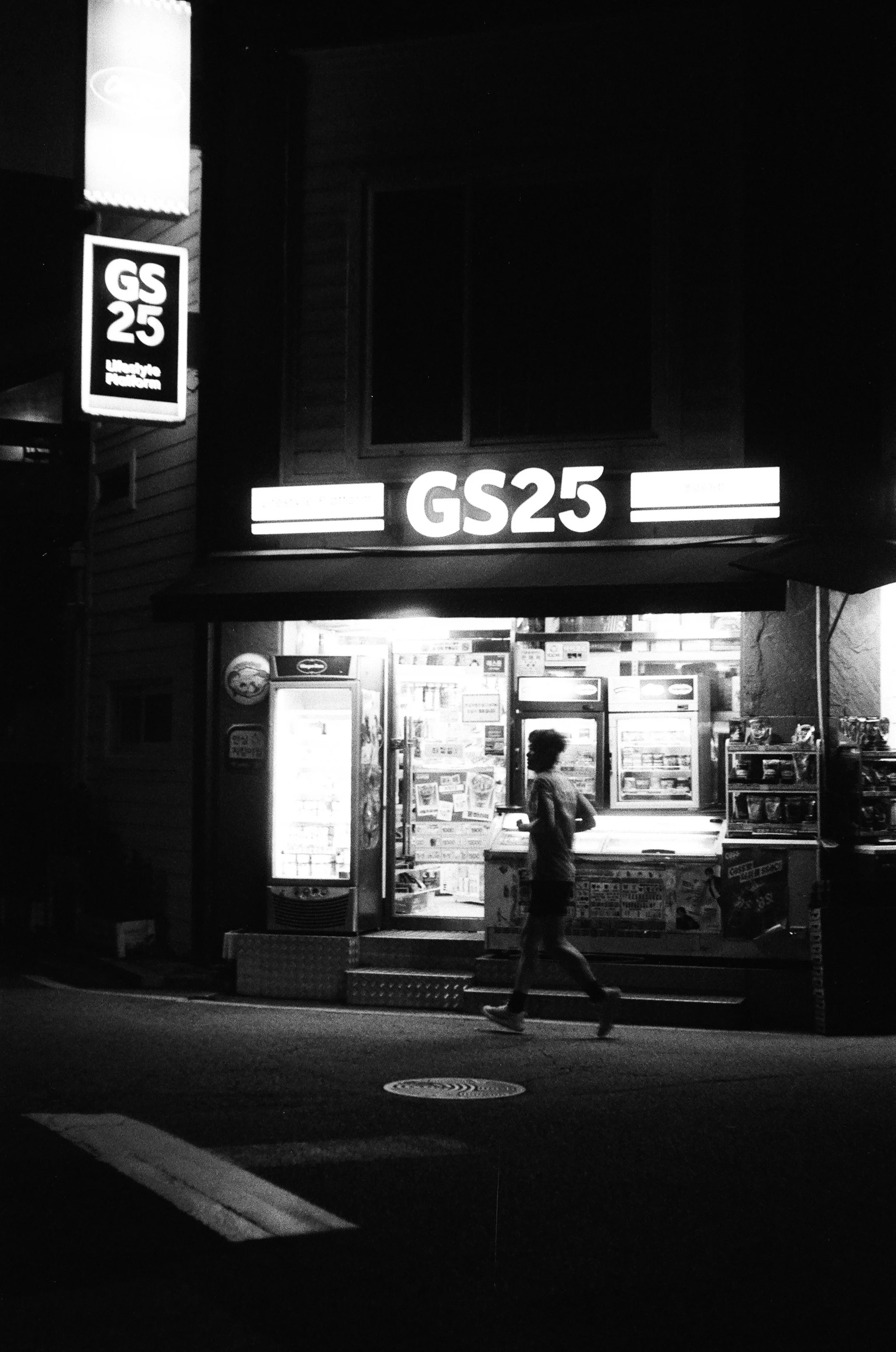 Man jogging in front of a Korean convenience store at night captured in black and white on film using the Industar 26m lens.