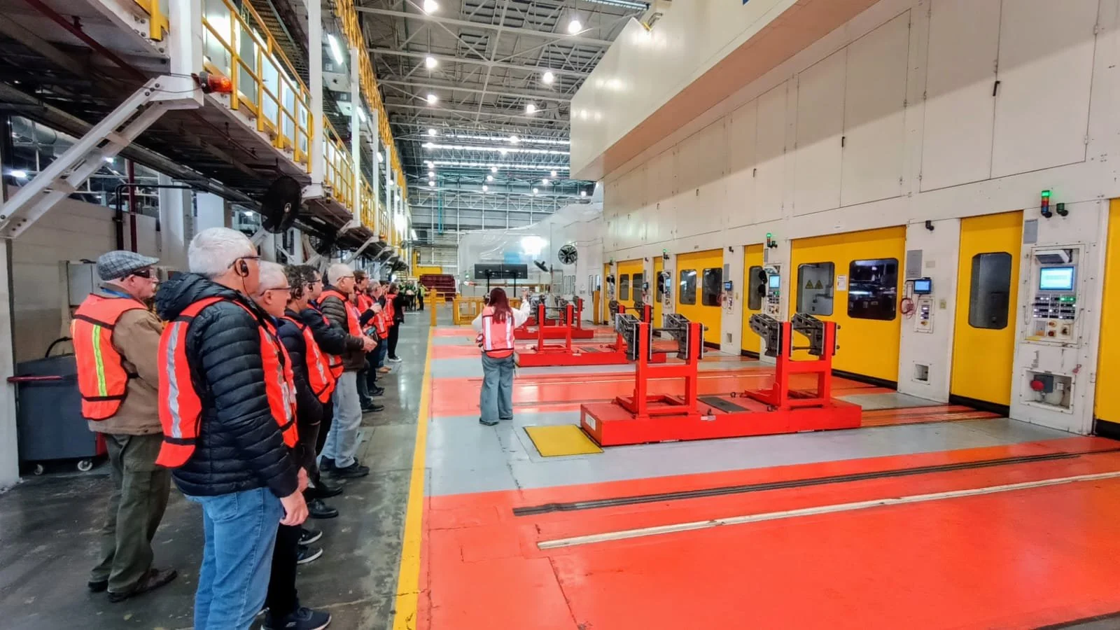 Grupo de personas observando una sala de fabricación o mantenimiento industrial con varias cabinas amarillas y equipos en un interior de fábrica.