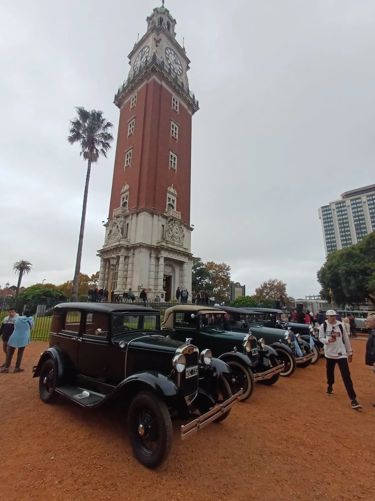 Plaza con reloj de Torre Latinoamericana, autos antiguos y personas. Montañas de fondo, día nublado.