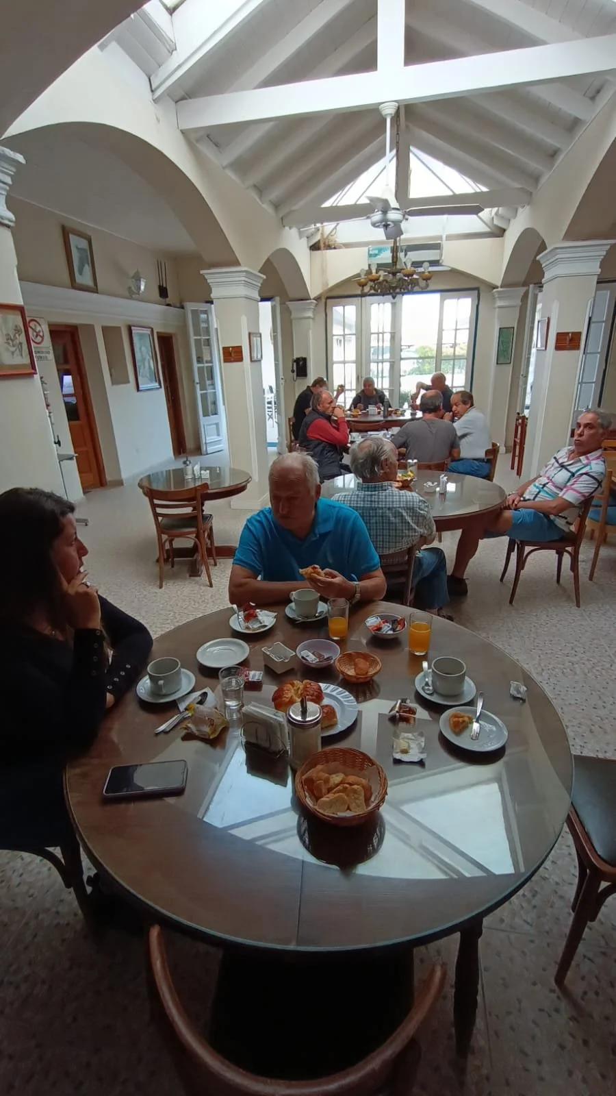 Personas desayunando en un restaurante con paredes blancas, ventanas grandes, techos altos y estructura de madera.