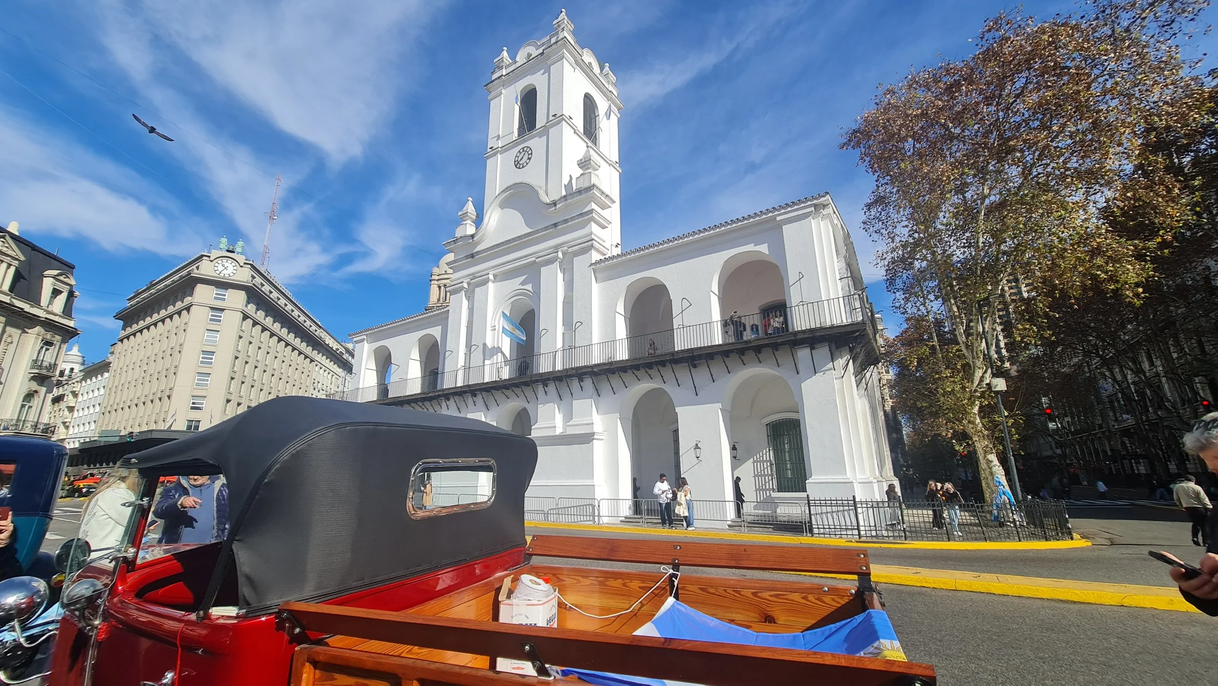 Iglesia blanca con torre en una ciudad, con árboles y edificios alrededor, y un cielo despejado.