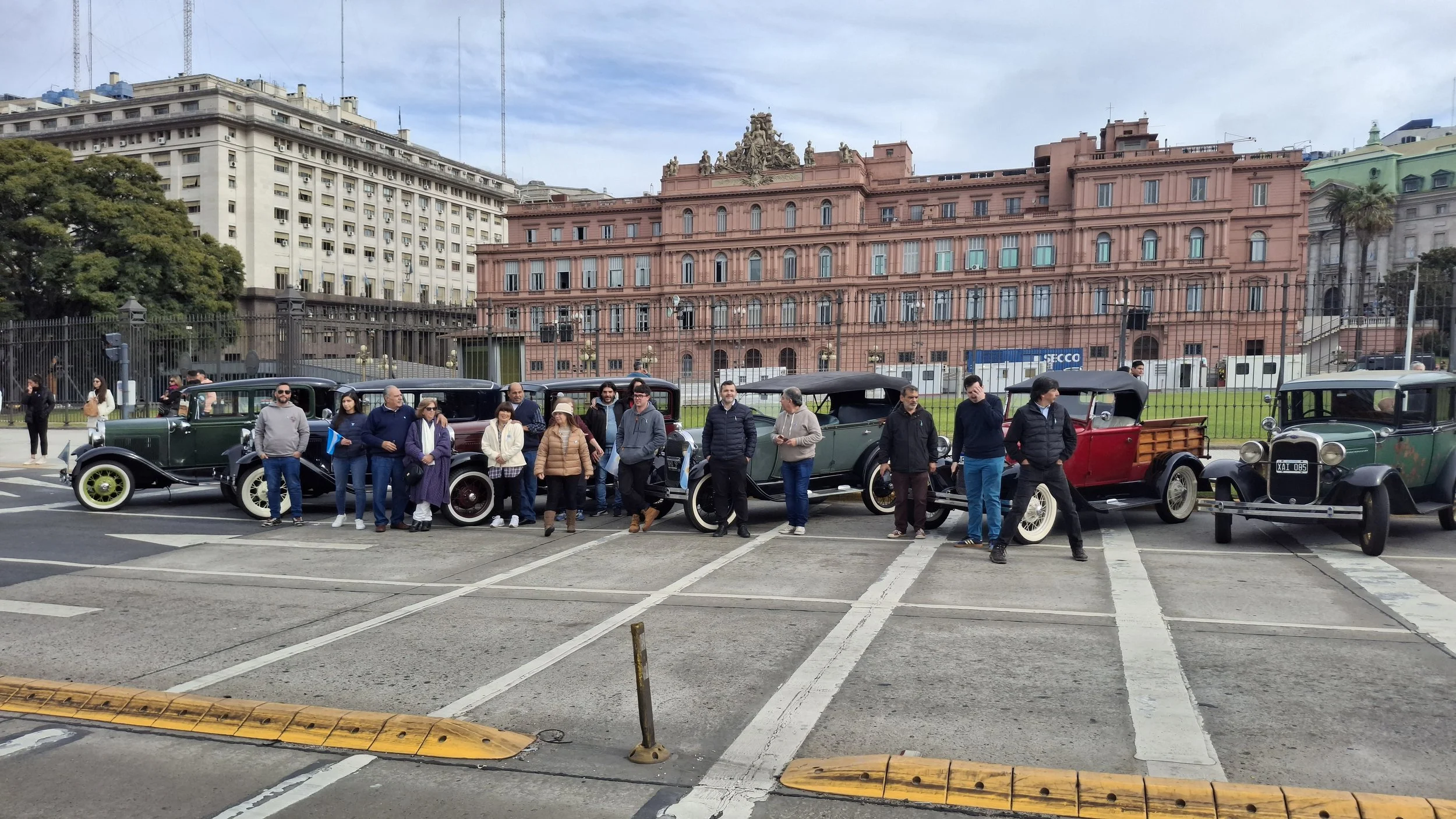 Grupo de personas posando frente a autos antiguos en frente del Palacio Nacional en Ciudad de México.