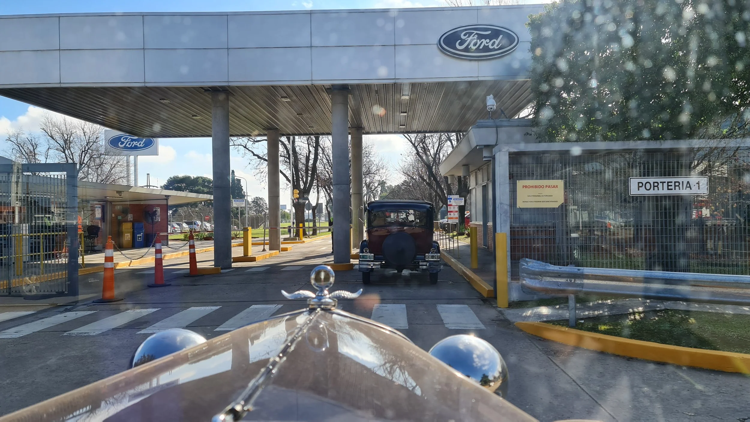 Entrada a una concesionaria Ford con señalización y un coche antiguo estacionado en el área de acceso.